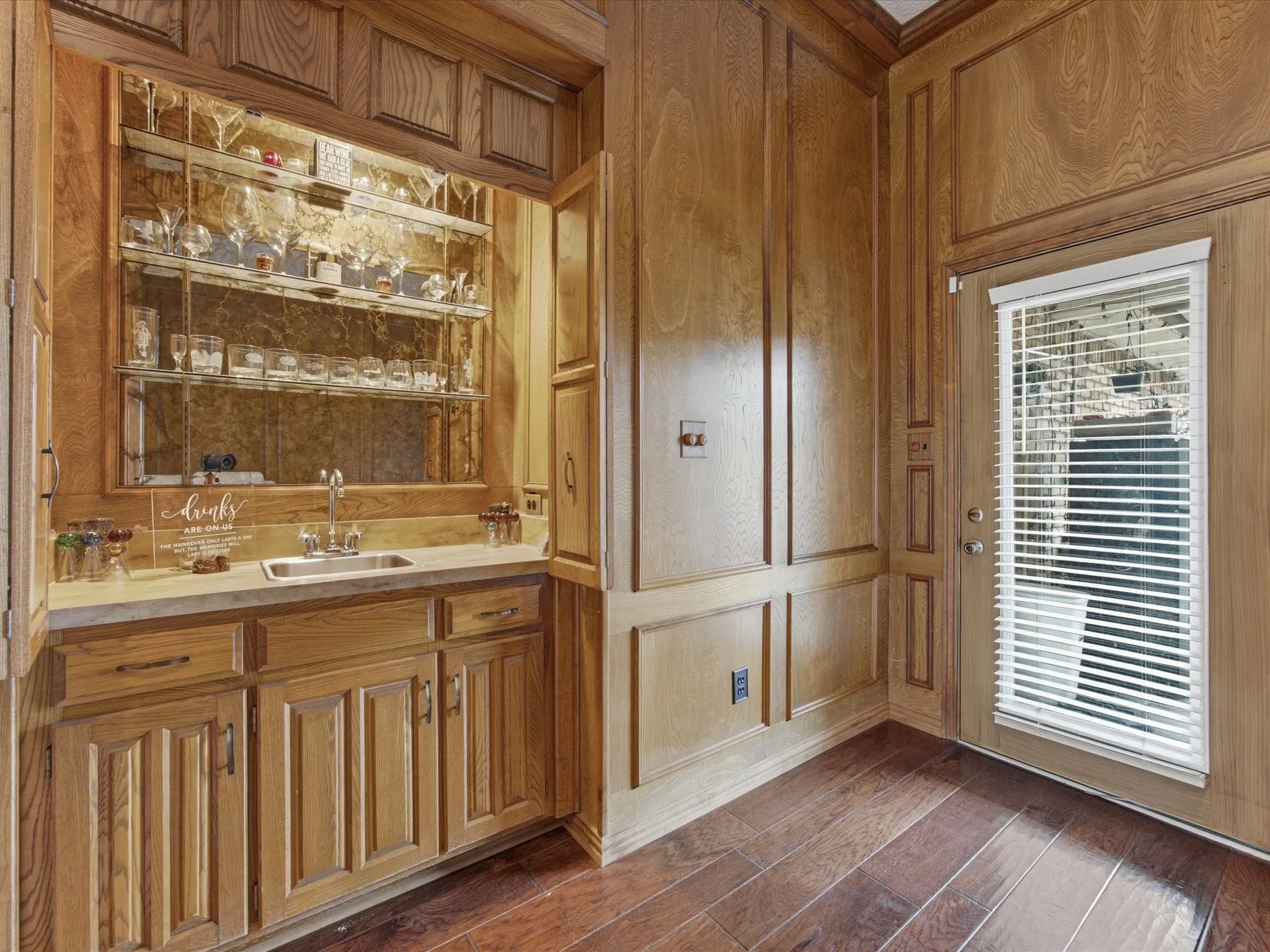 Custom built-in wet bar featuring a stainless steel sink, mirrored backsplash, and glass shelving