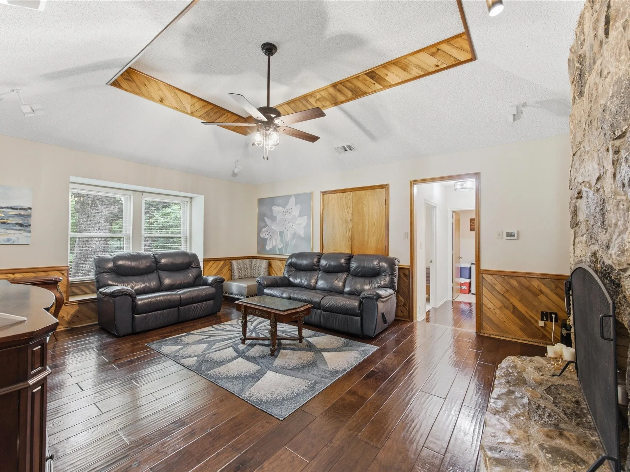 Living area featuring wood-finish flooring, a stone-faced fireplace, and wainscoting