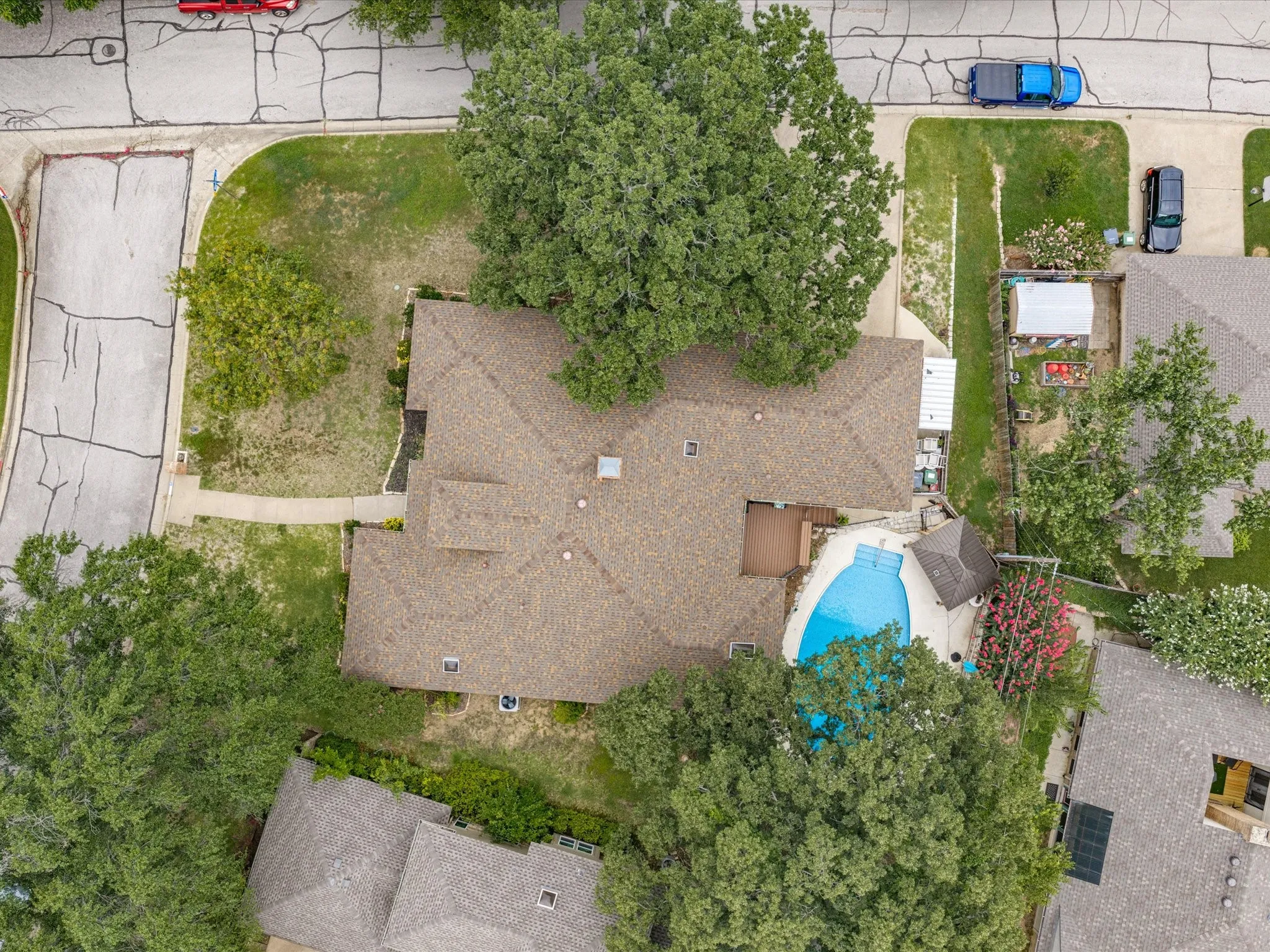 Residential property featuring a shingle roof, mature trees, a curvilinear swimming pool, and a poolside deck