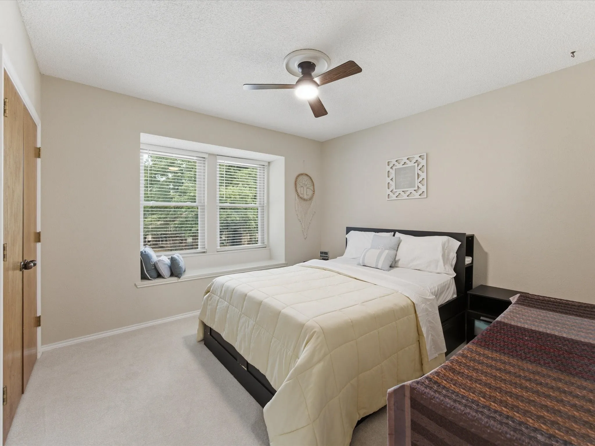 Recessed window alcove with integrated sill seating, light carpet flooring, and a ceiling fan with integrated lighting
