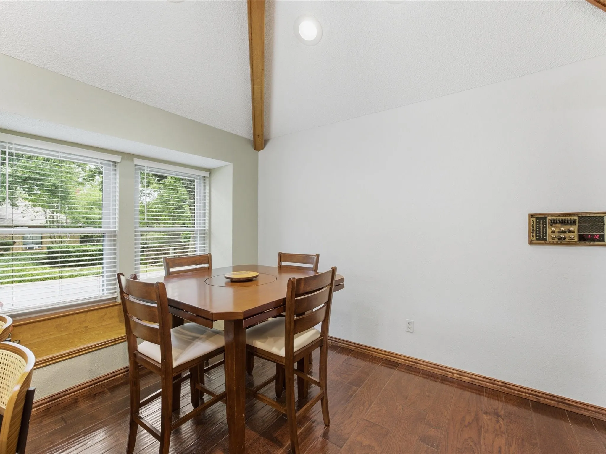Dining area featuring wood-finish flooring, a vaulted ceiling with exposed wood beam, recessed lighting, and a bay window with blinds
