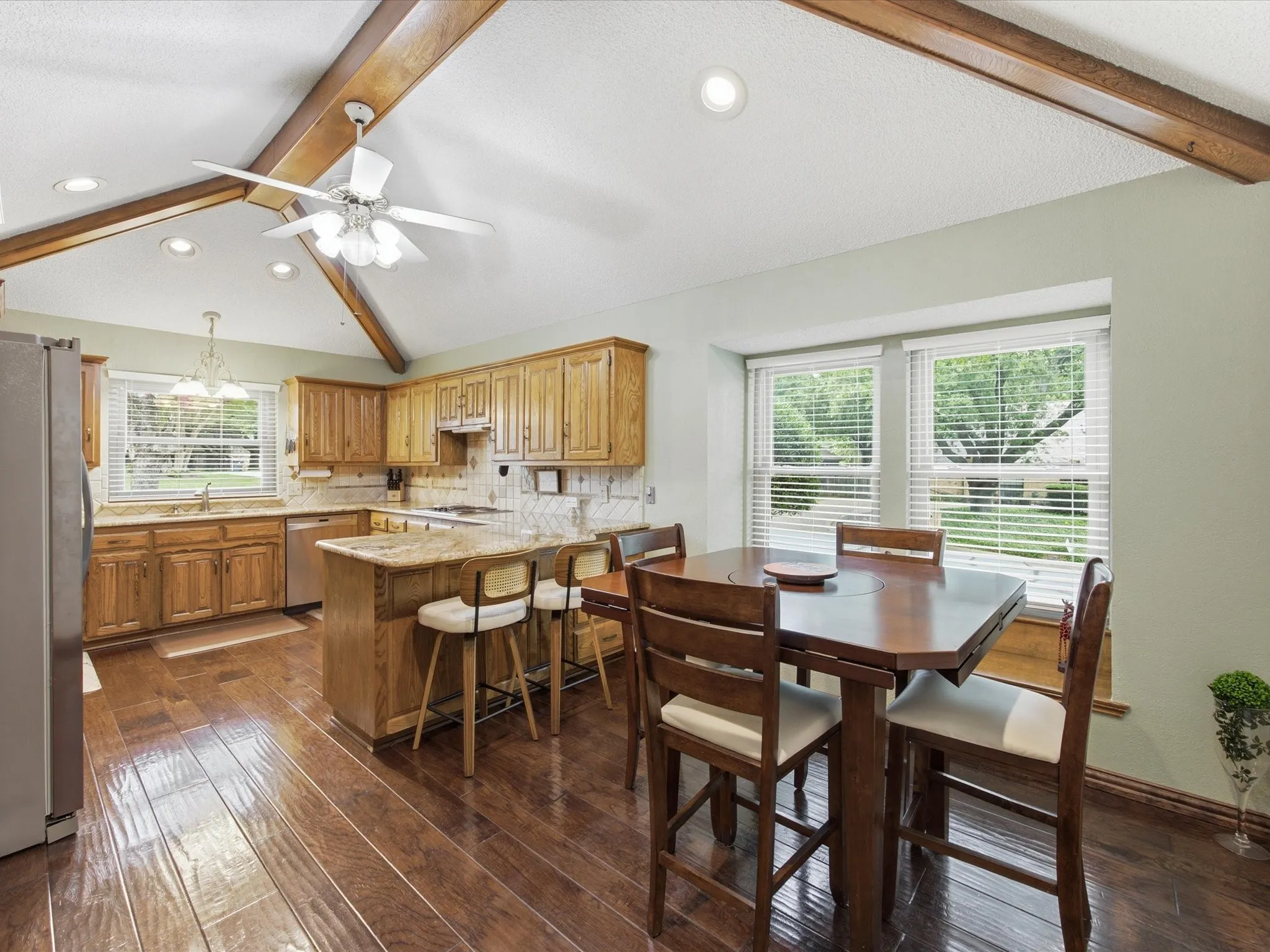 Kitchen featuring wood-finish flooring, vaulted ceiling with exposed wood beams, wood cabinetry, light-toned countertops, and a window with horizontal blinds