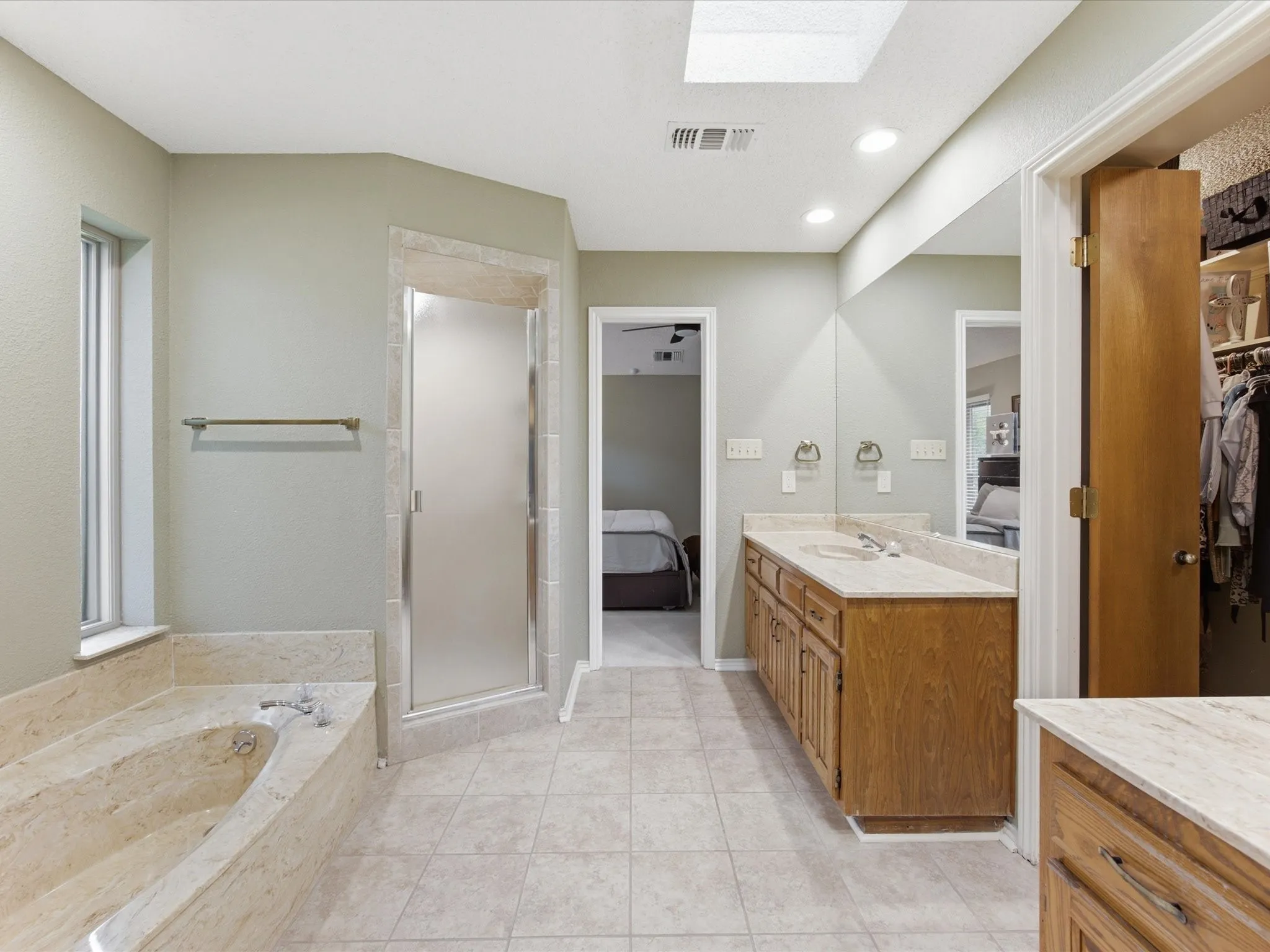 Primary Bathroom featuring a skylight, tile flooring, a built-in tub with stone surround, a glass-enclosed shower, and a dual vanity with a light-toned countertop