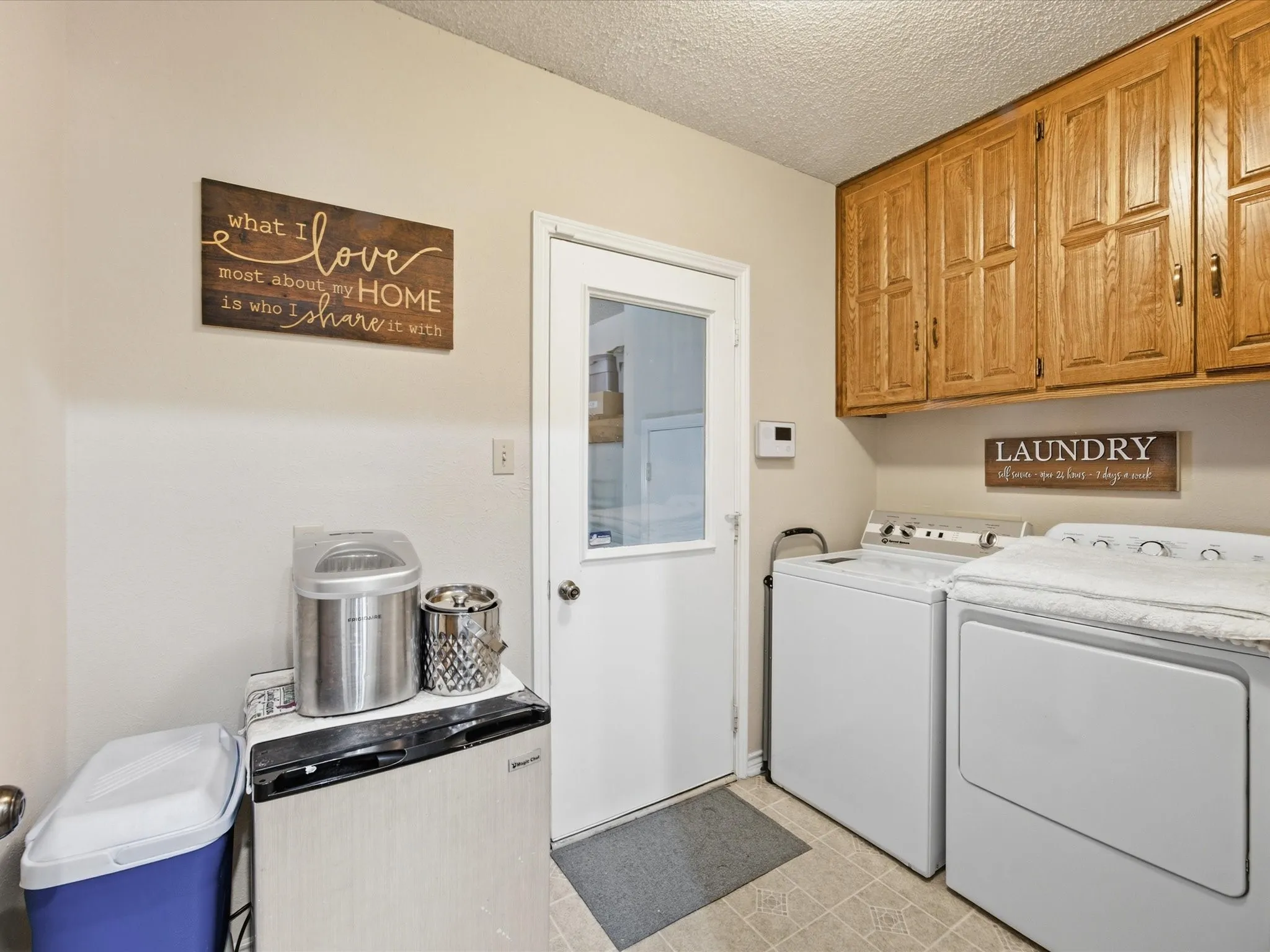 Laundry area featuring wood-finish cabinetry, a white paneled door with a clear glass insert, and light-toned vinyl flooring
