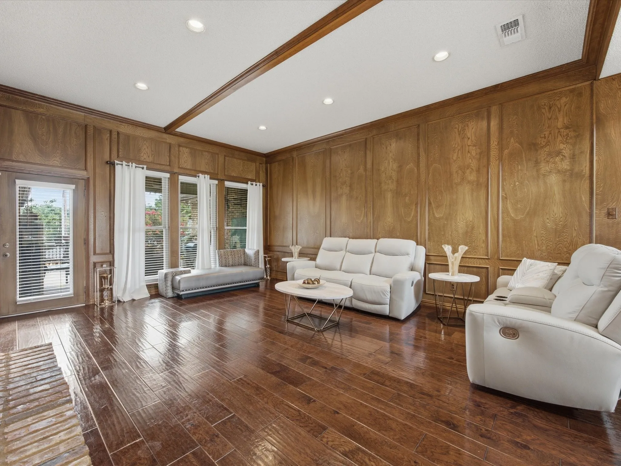 Spacious room featuring wood-finish flooring, wood paneling with decorative trim, recessed lighting, and multiple windows with blinds