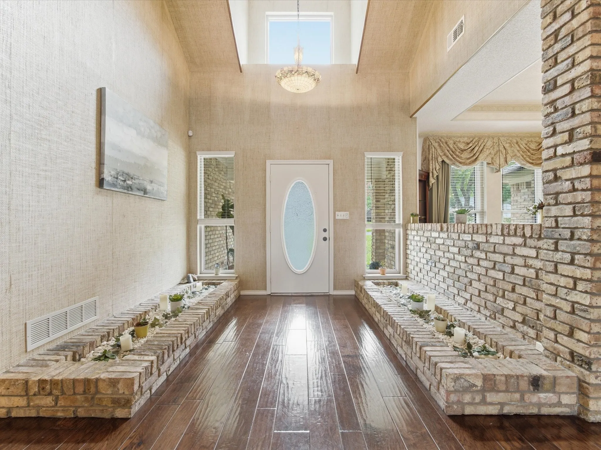 Entryway featuring wood-finish flooring, a white oval-paneled door, and two brick-built planter boxes