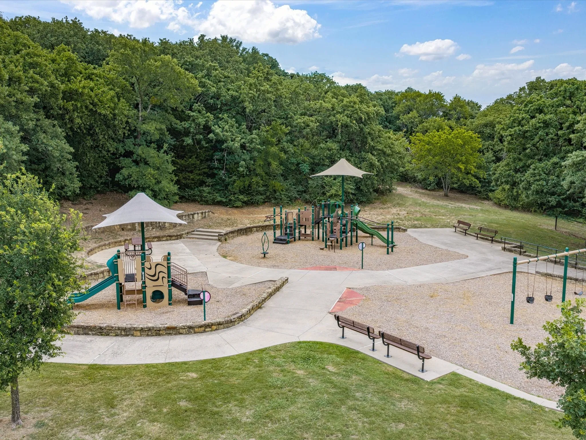 Community playground featuring multiple play structures with sunshades, swings, and benches