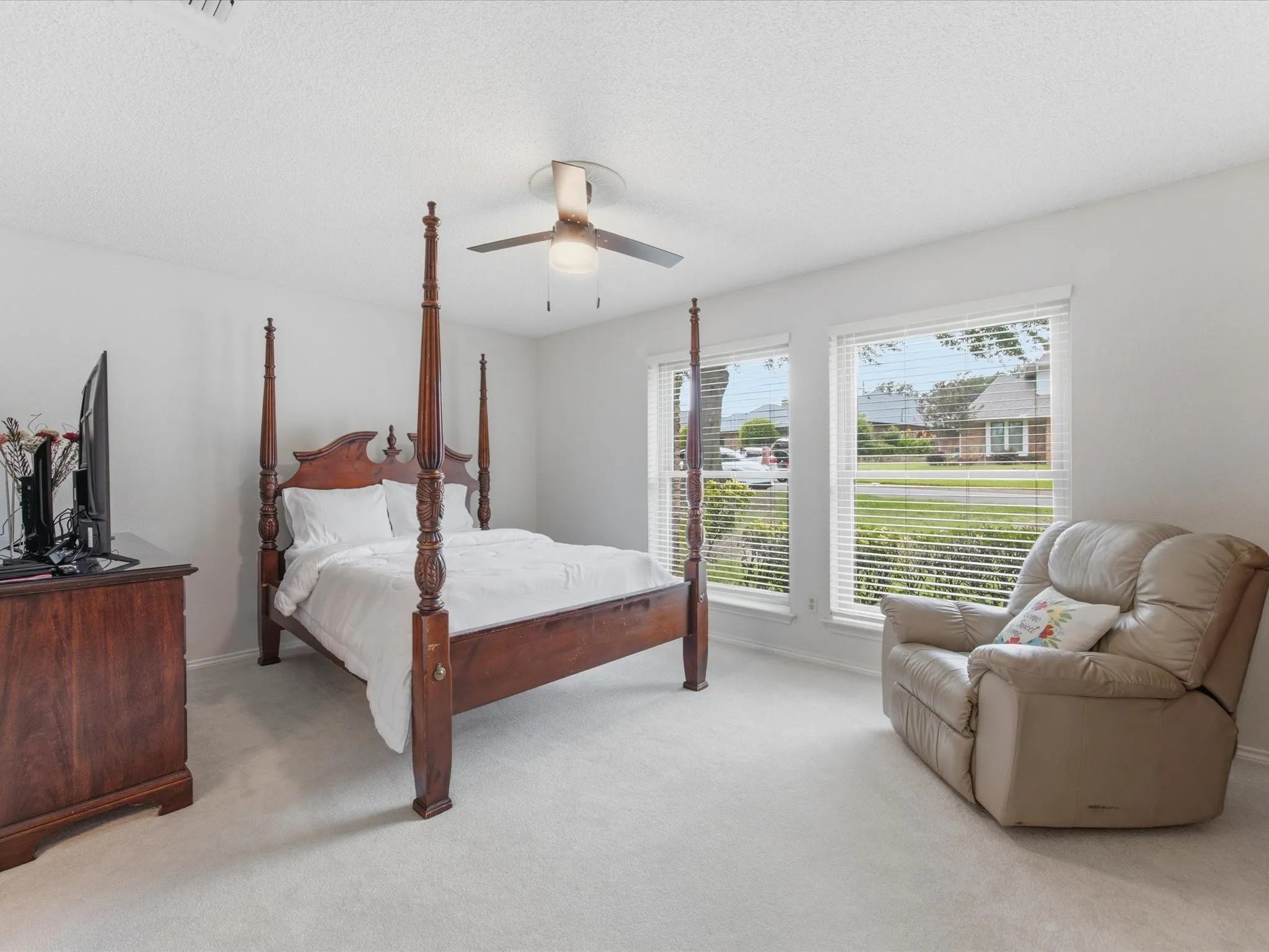 Bright bedroom featuring light-colored carpet, white walls, two windows with blinds, and a ceiling fan with light fixture