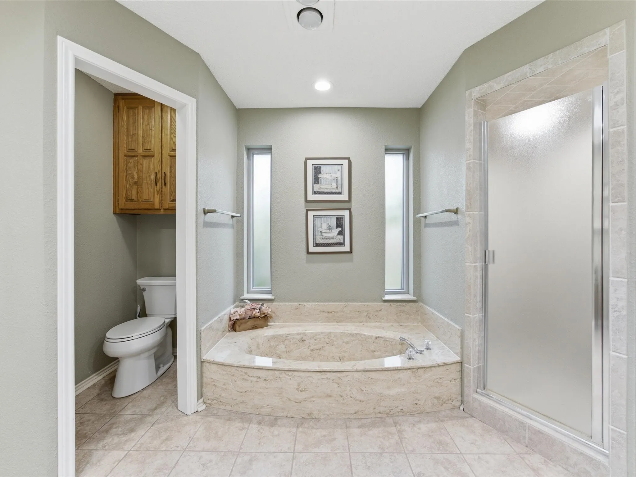 Primary Bathroom featuring a tiled soaking tub with marble-finish surround, a tiled walk-in shower with frosted glass enclosure, and light-colored tile flooring