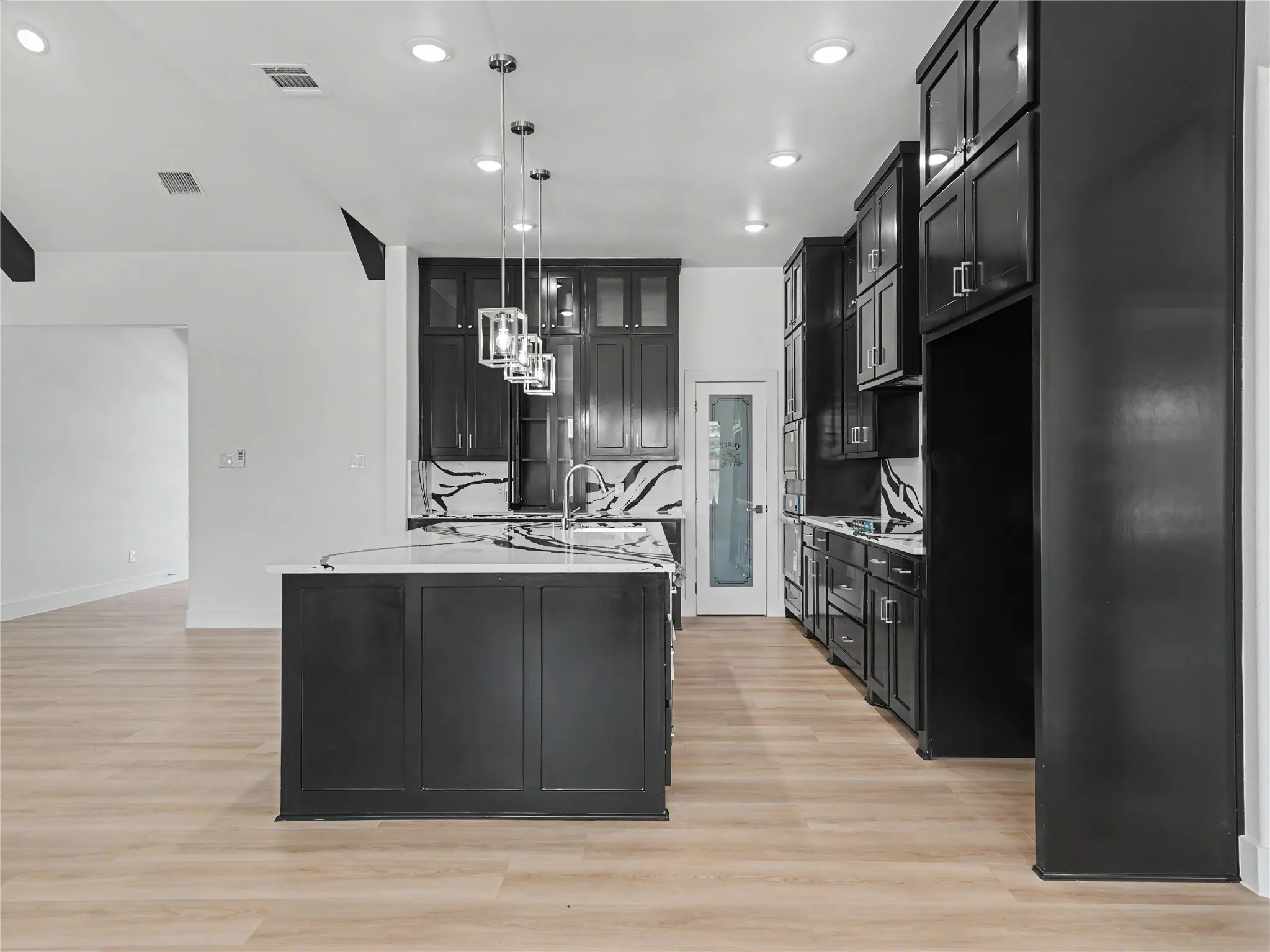 Kitchen featuring a central island with a sink, pendant lighting, dark cabinetry, light countertops, and wood-finish flooring