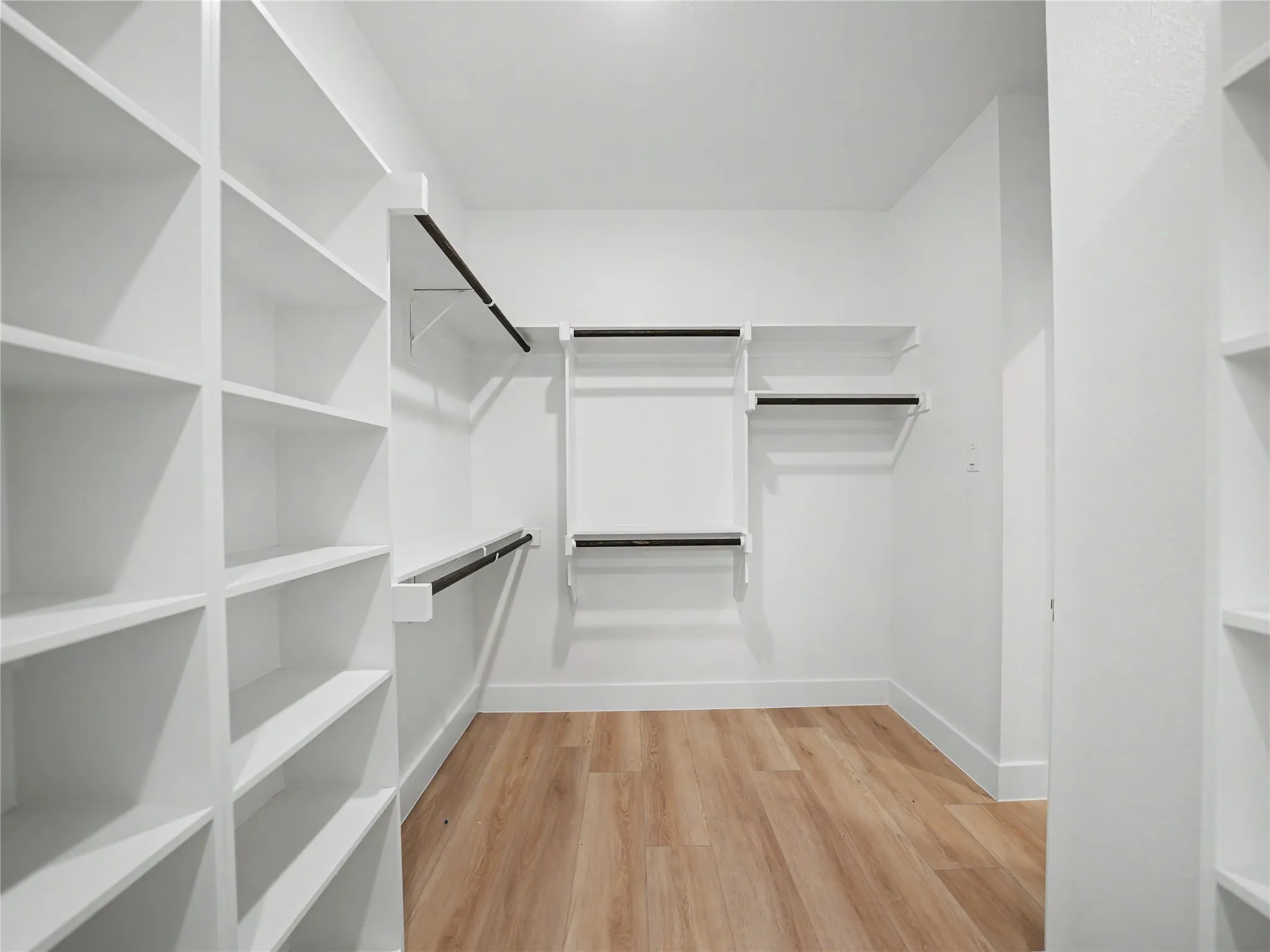 Walk-in closet featuring extensive built-in shelving, multiple hanging rods, crisp white finishes, and wood-finish flooring