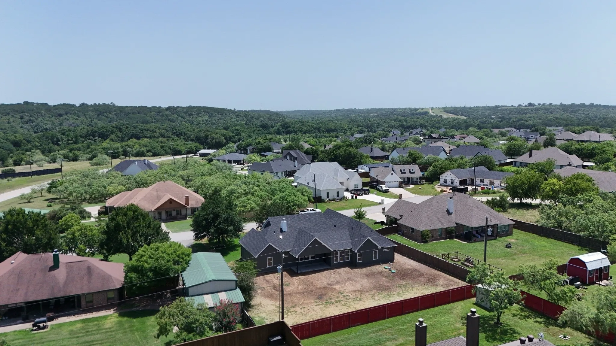 New construction residence featuring a dark shingle roof, light-colored siding, and a red perimeter fence