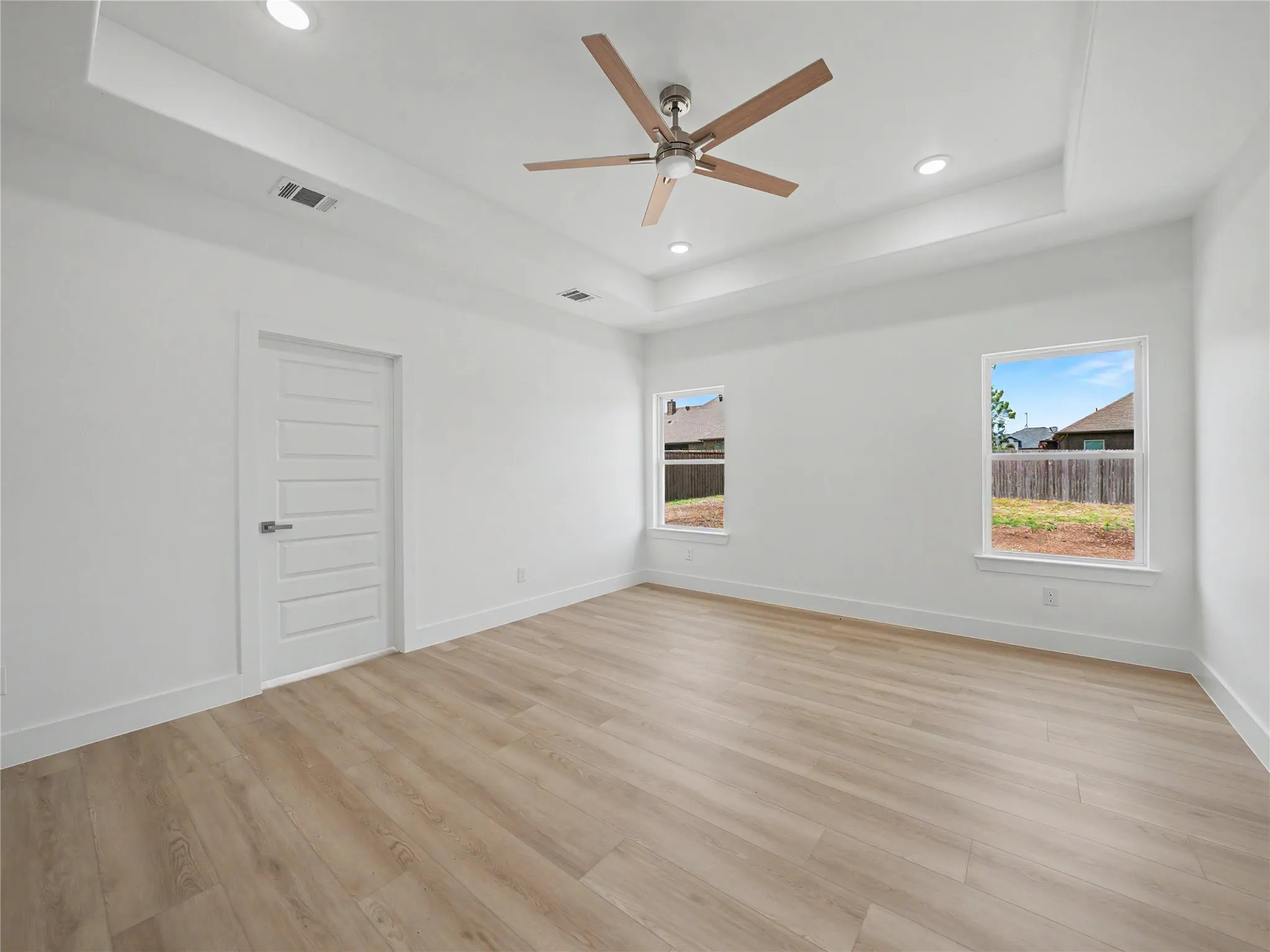 Spacious interior room featuring a tray ceiling with recessed lighting and a ceiling fan