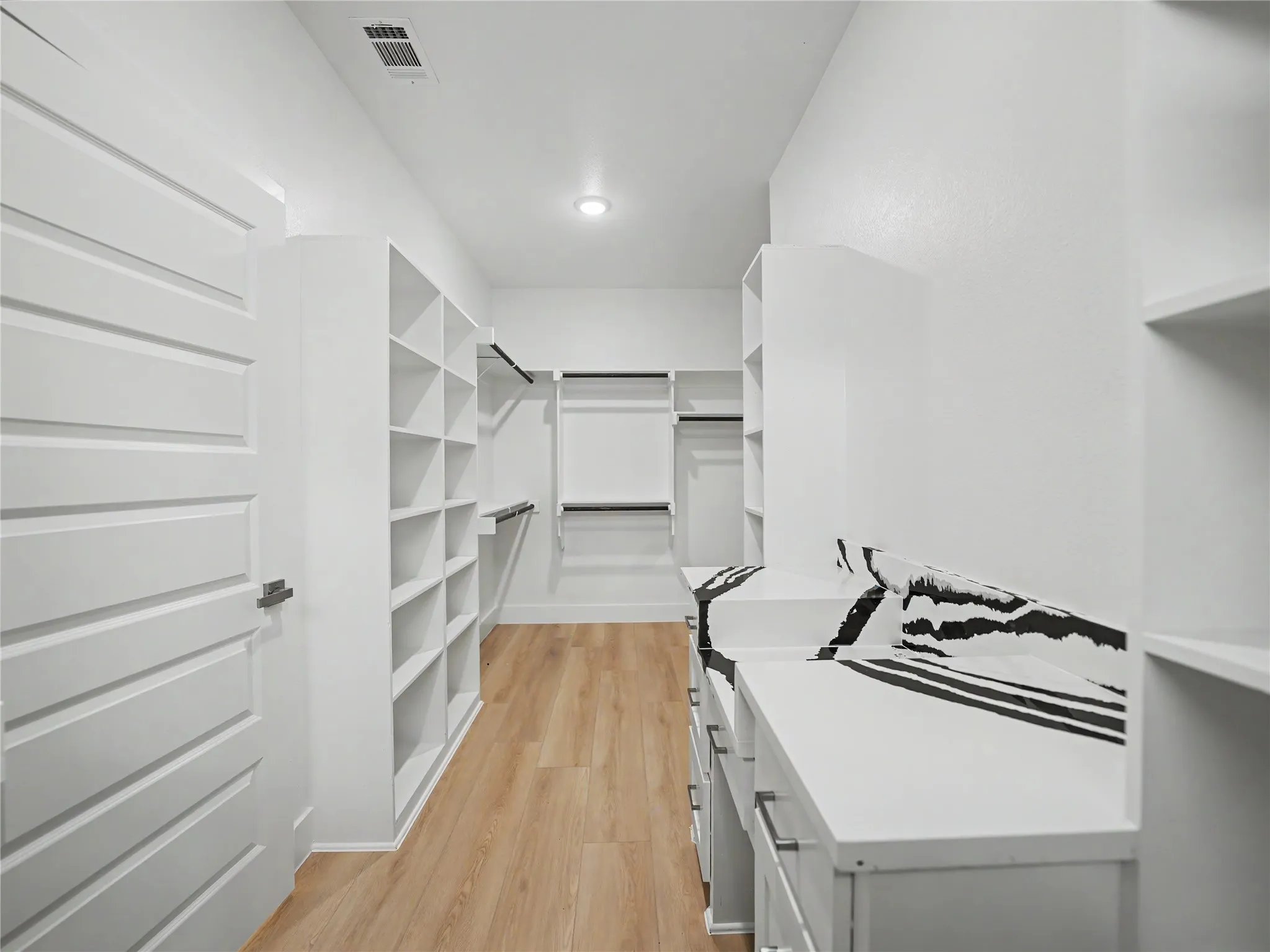 Custom closet system with extensive shelving, multiple hanging rods, built-in drawers, wood-finish flooring, and a modern paneled door