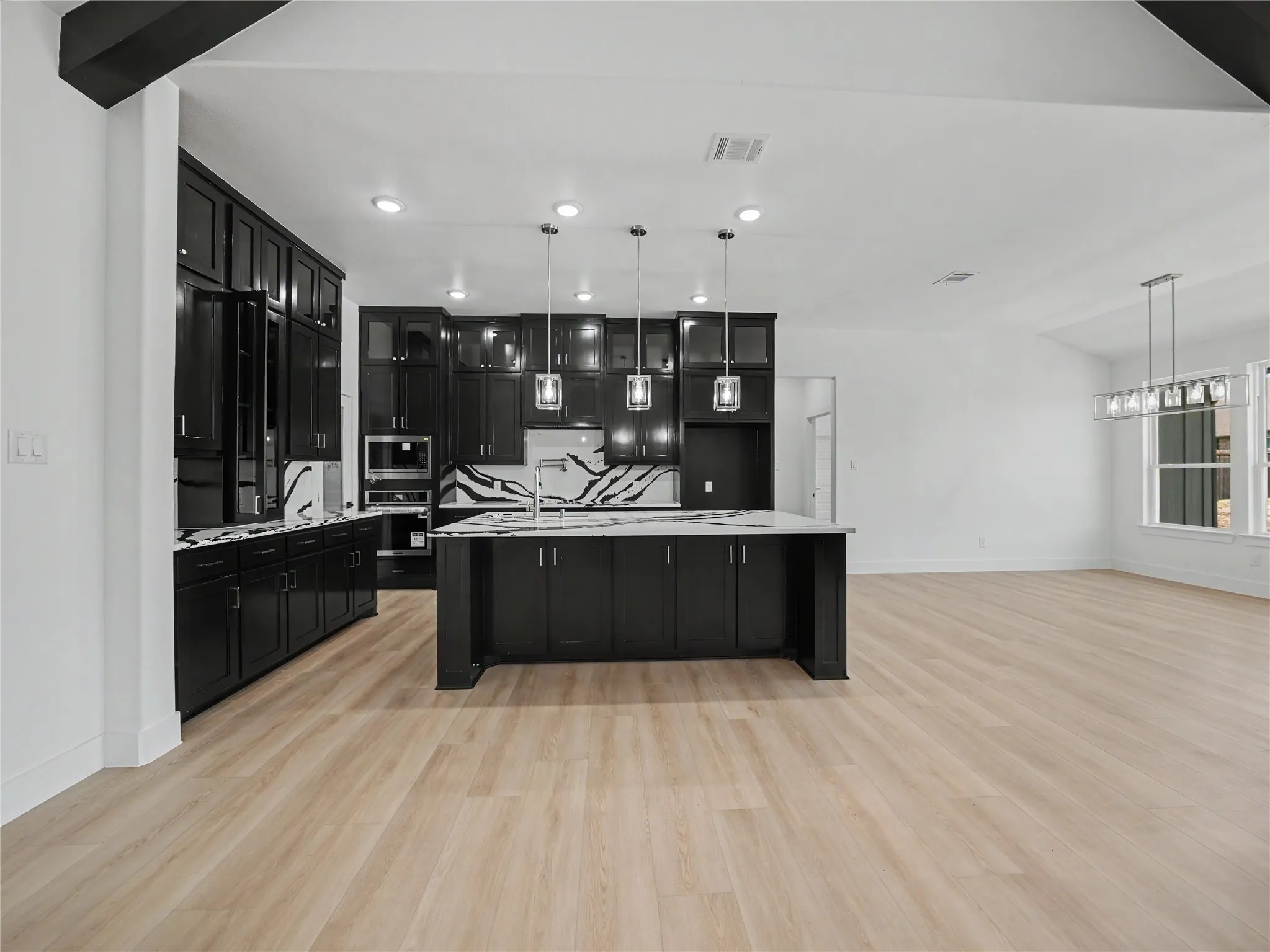 Modern kitchen featuring dark cabinetry, a central island with a sink, white countertops, and a patterned backsplash