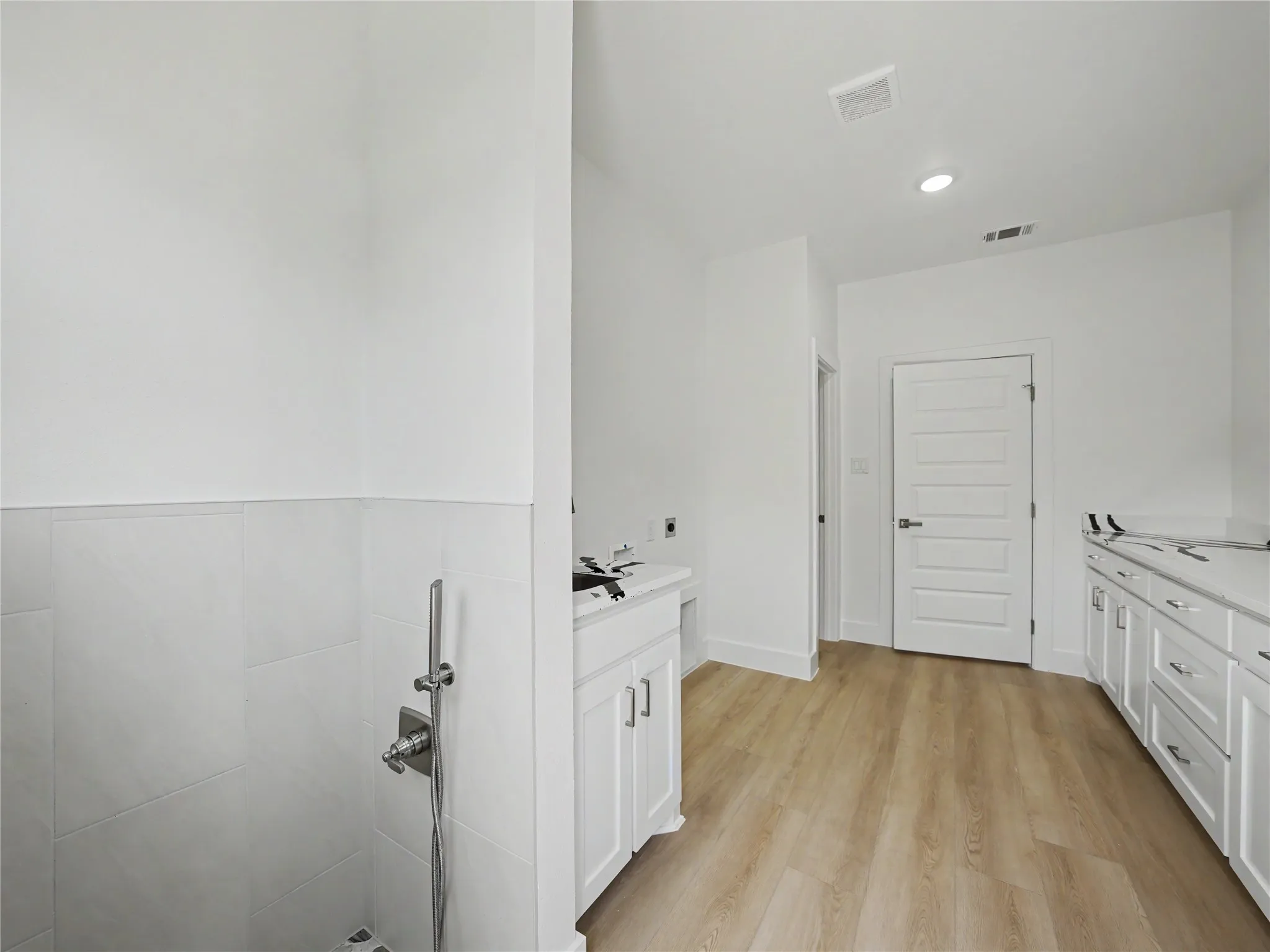 Laundry room featuring wood-finish flooring, white cabinetry, integrated sink, and tiled walls