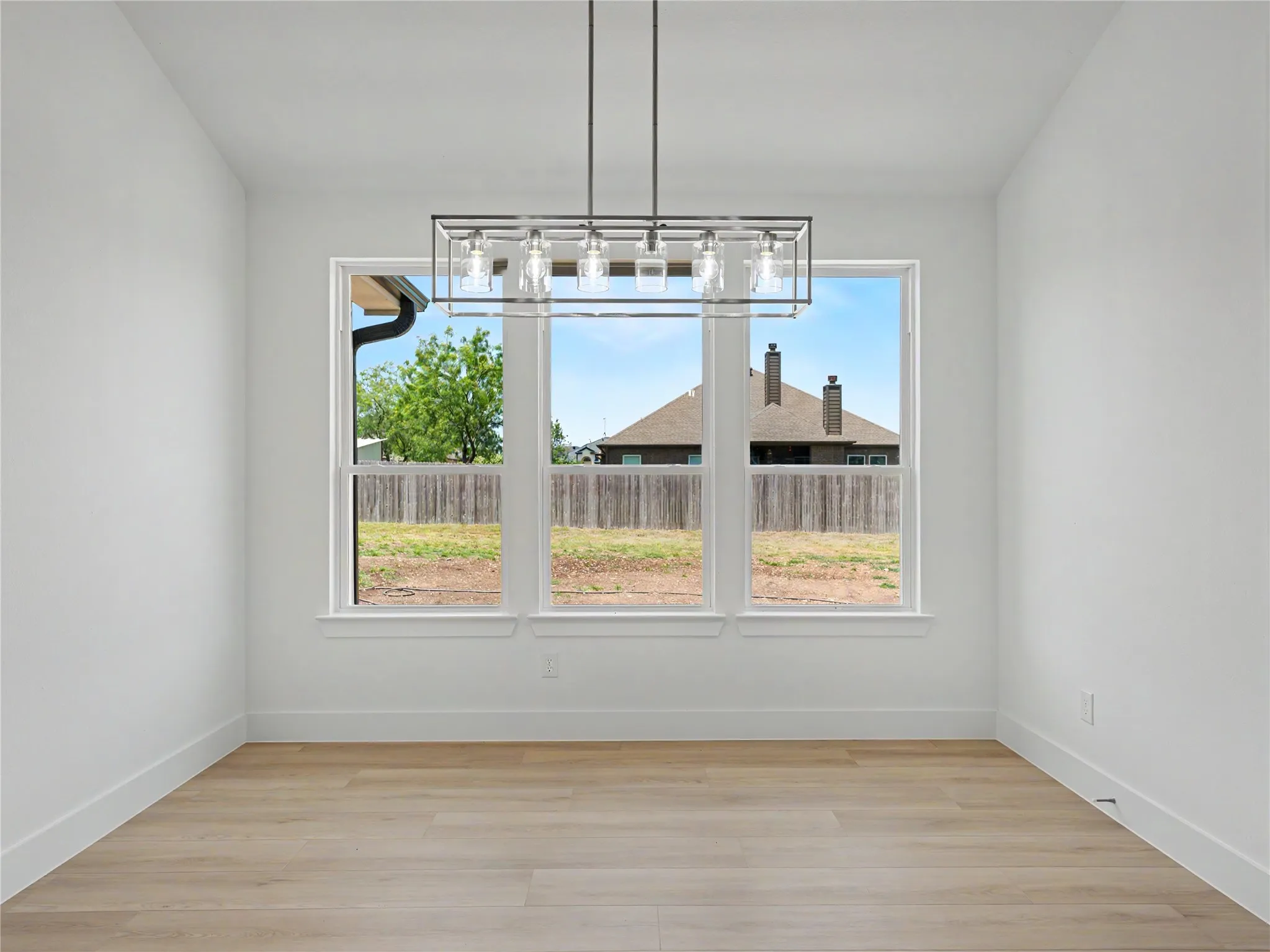 Dining area featuring a contemporary linear chandelier, three large windows, wood-finish flooring, white walls, and white trim