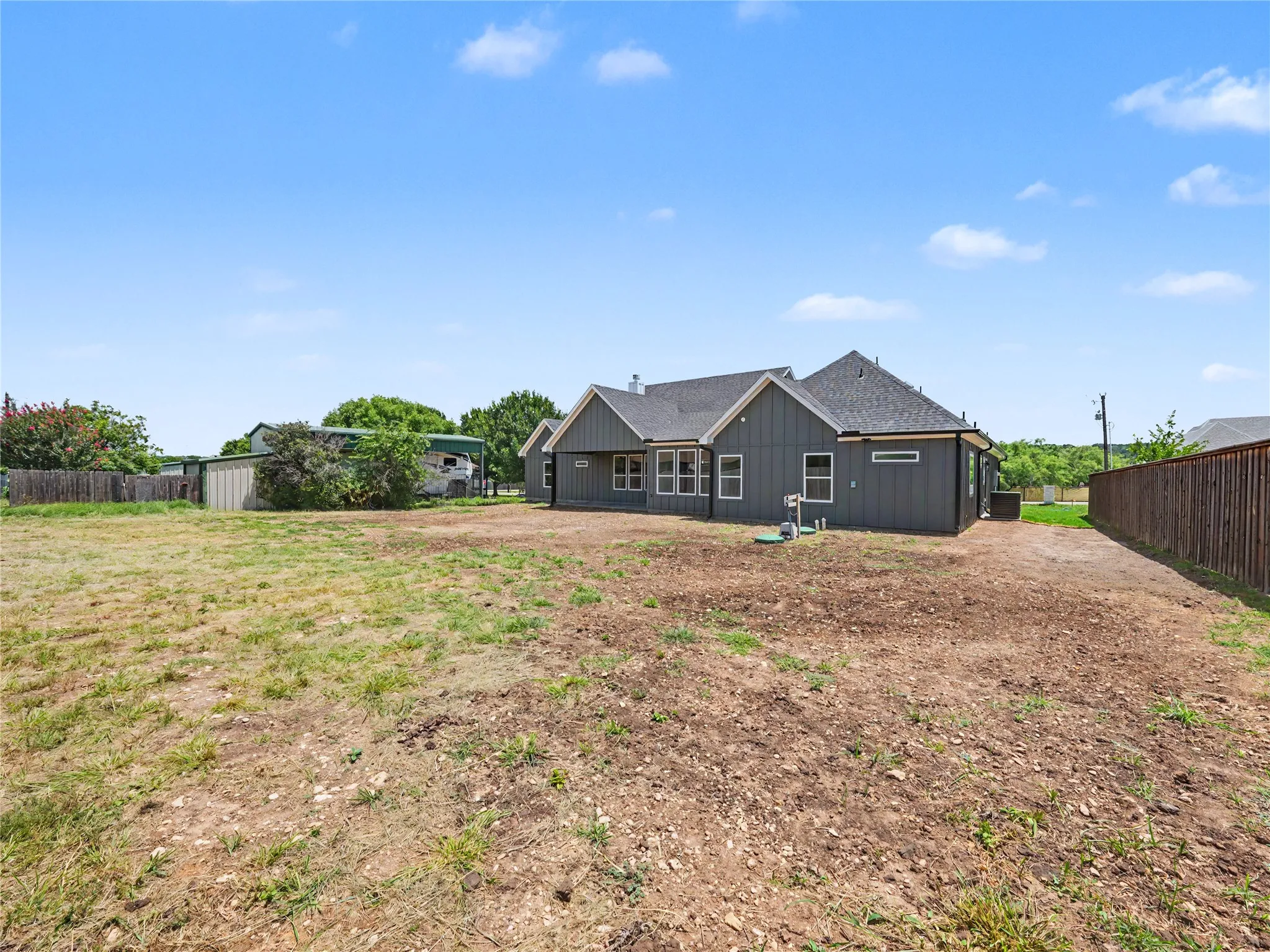 Expansive rear property with a dark-tone siding residence featuring multiple windows and a dark shingle roof