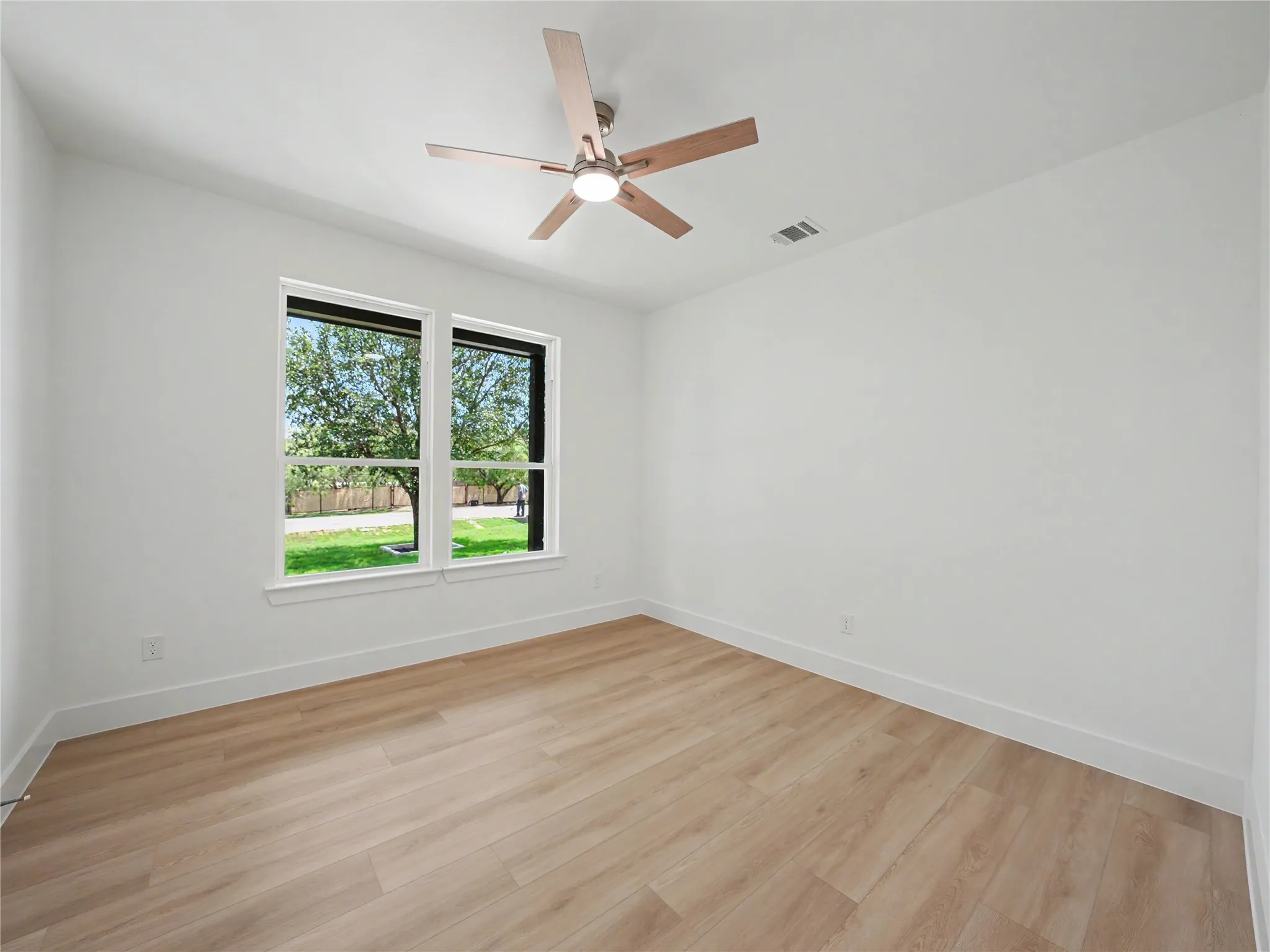Spacious room featuring wood-finish flooring, crisp white walls, and a contemporary ceiling fan