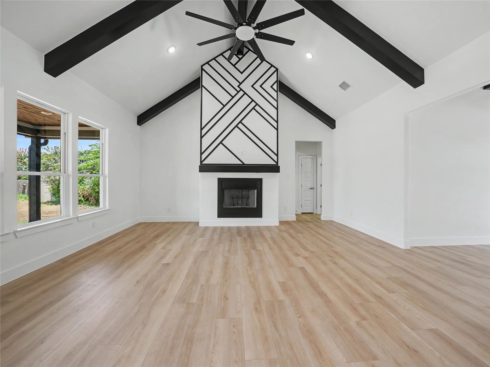 Spacious living area featuring a vaulted ceiling with exposed black beams, a decorative fireplace with a geometric mantel, and wood-finish flooring