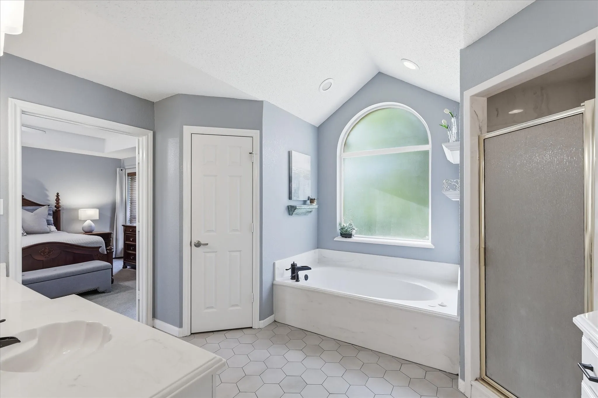 Bathroom featuring a built-in soaking tub under an arched window, a stand-up shower with a glass enclosure, and hexagonal tile flooring