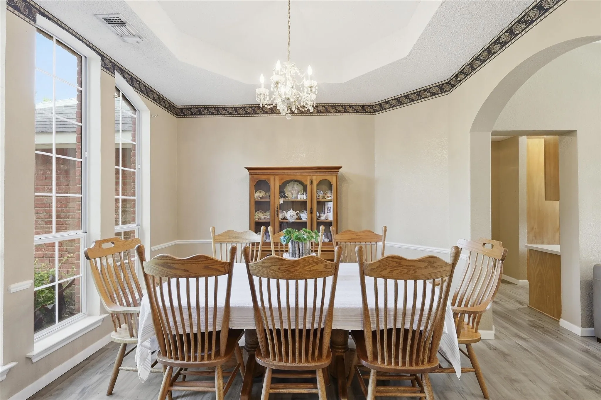 Dining area featuring a tray ceiling with decorative trim, large bay windows, a crystal chandelier, and wood-finish flooring