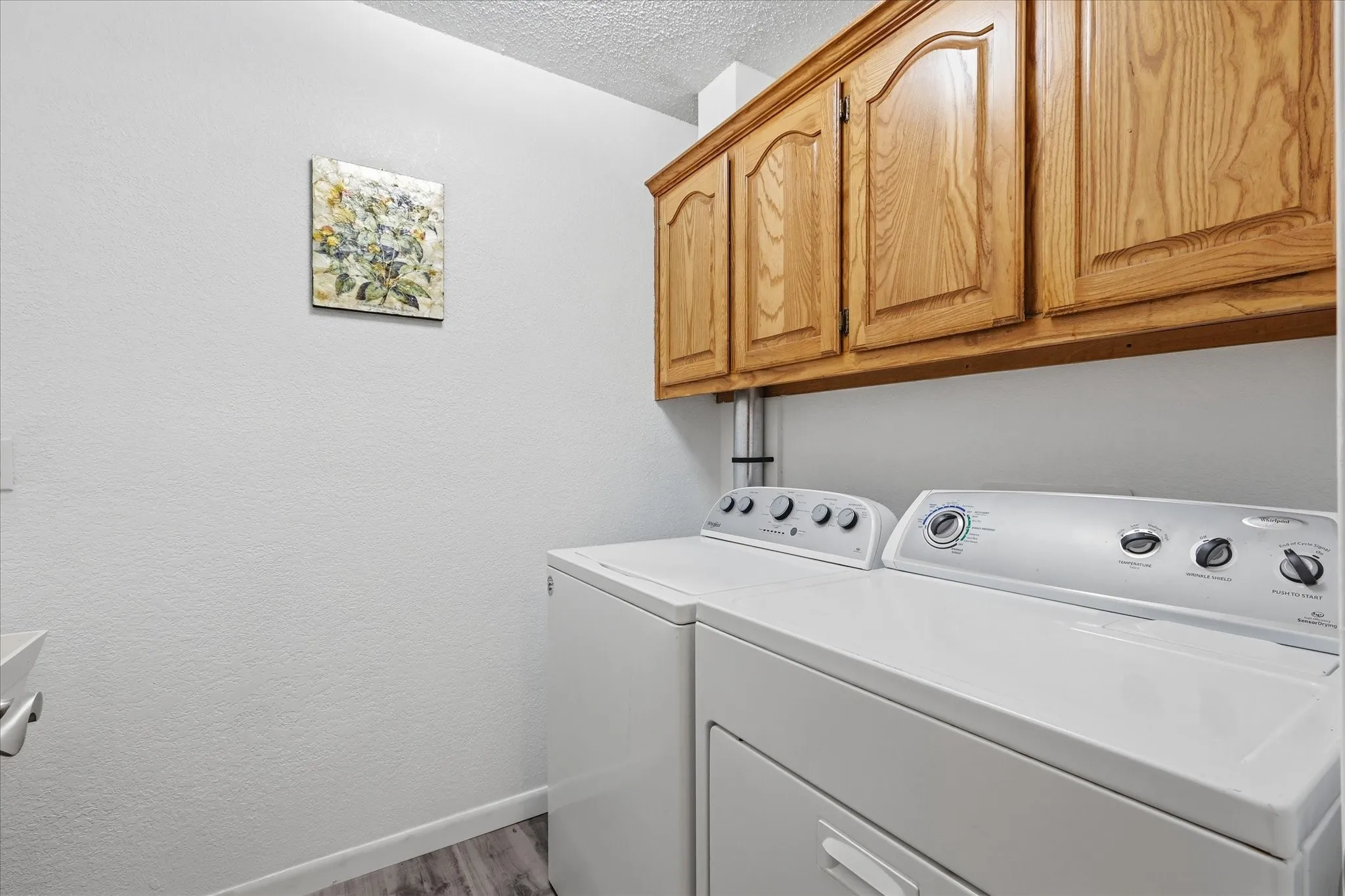 Laundry area featuring overhead wood cabinetry and wood-finish flooring