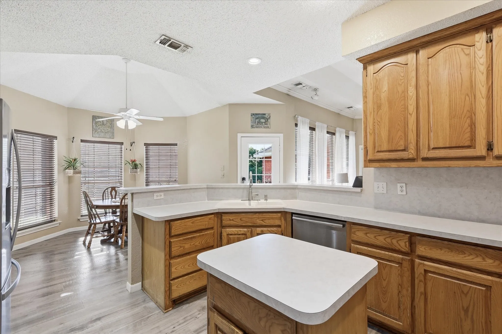 Kitchen featuring wood-finish cabinetry, white countertops, stainless steel dishwasher, and a central island