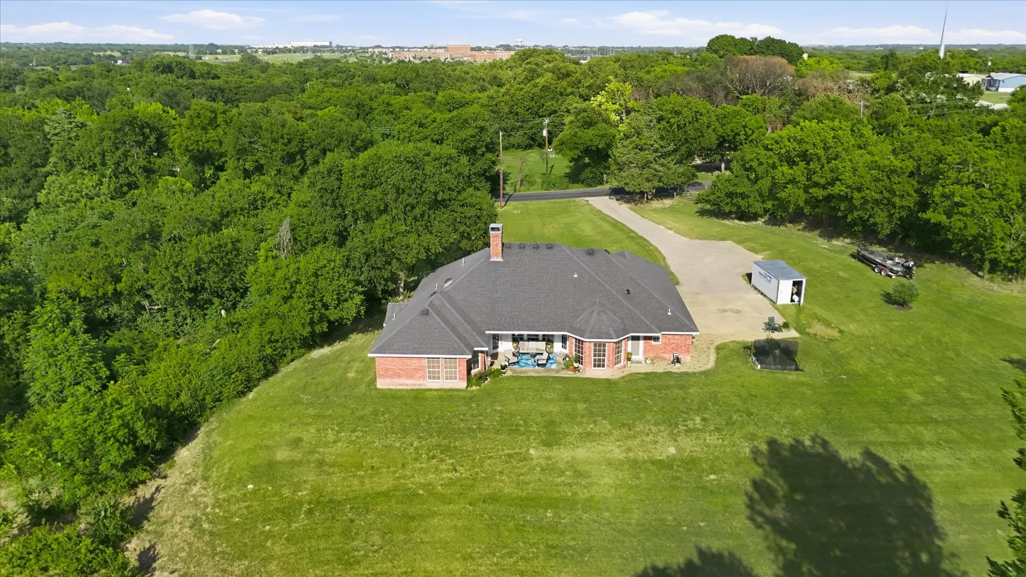 Expansive property featuring a brick exterior home with a dark shingle roof, surrounded by mature trees