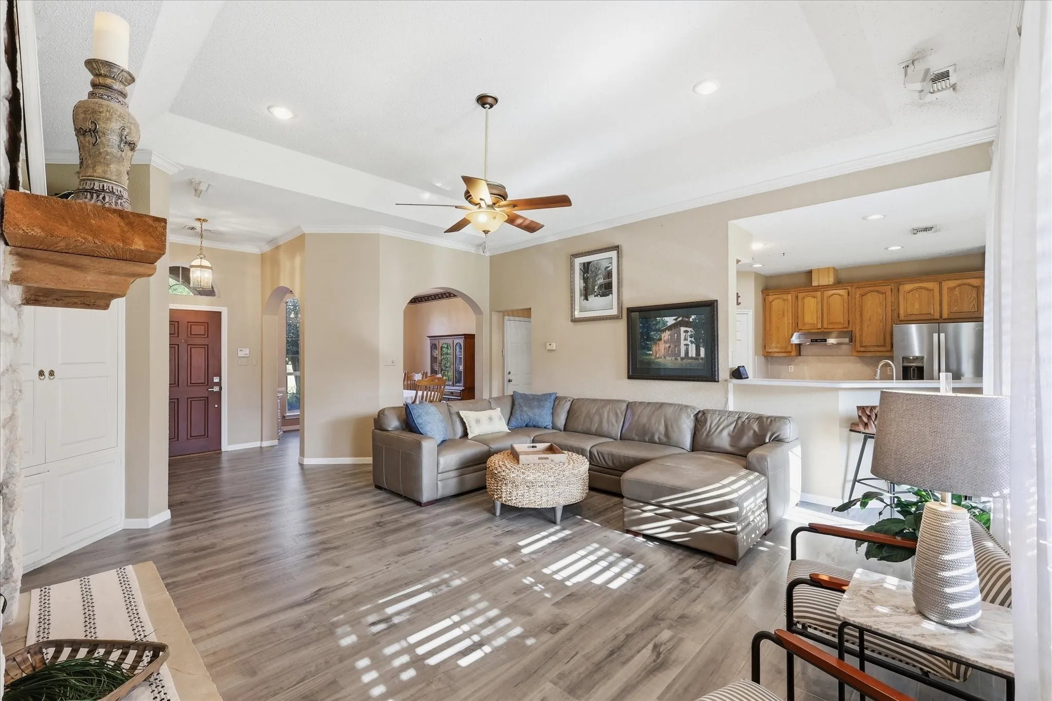 Spacious living area featuring wood-finish flooring, a tray ceiling with recessed lighting, and a ceiling fan
