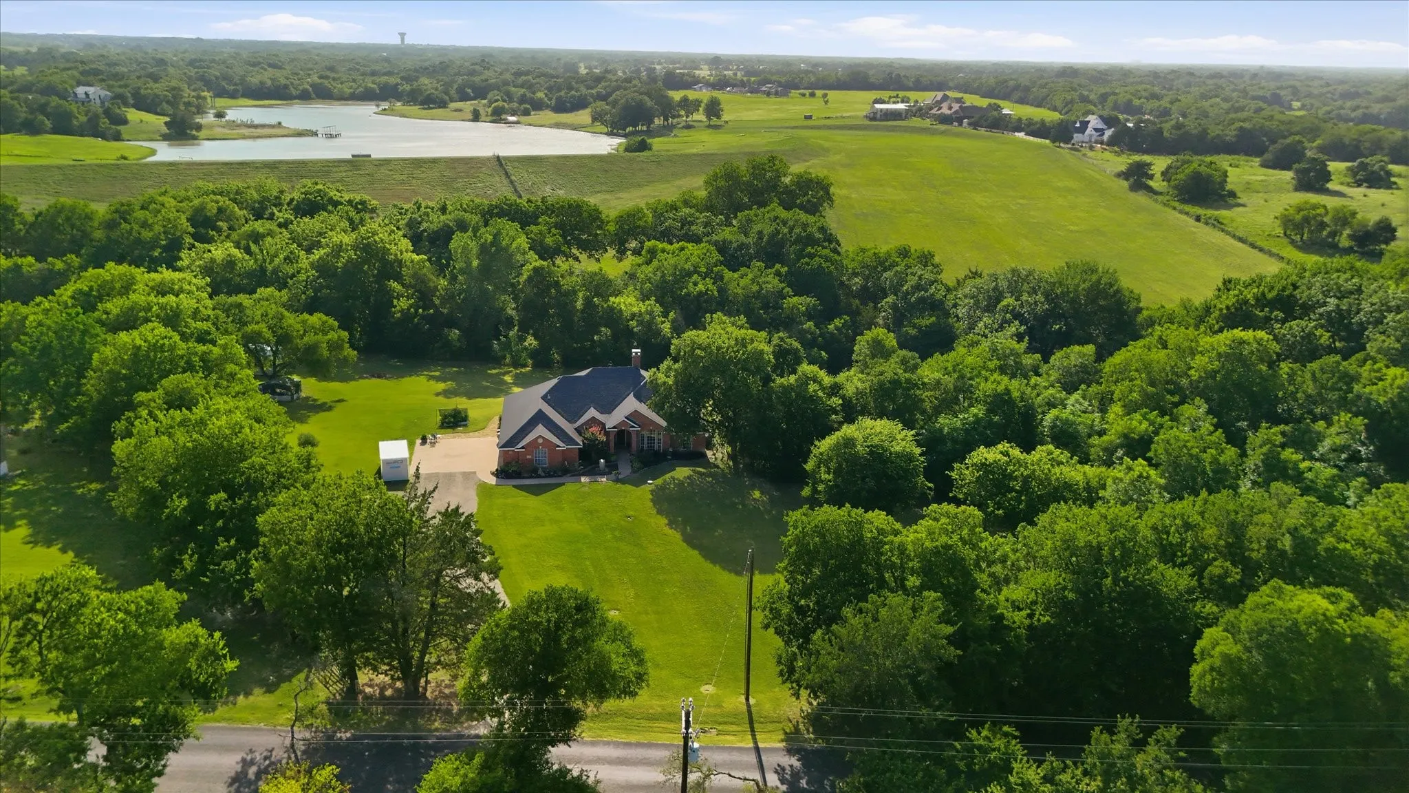 Sprawling property featuring a single-story brick residence with a dark roof and prominent gables, surrounded by mature trees and expansive green lawns