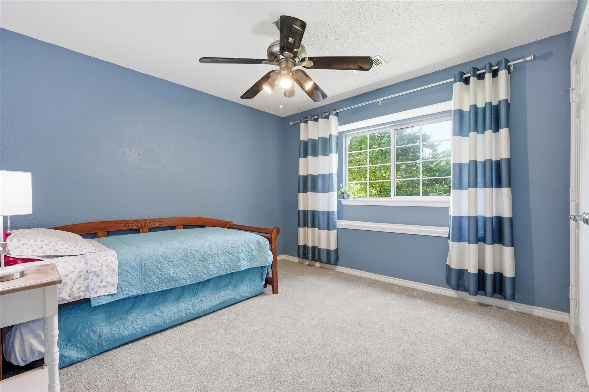 Room featuring light blue walls, soft grey carpeting, a multi-pane window, and a ceiling fan with integrated lighting