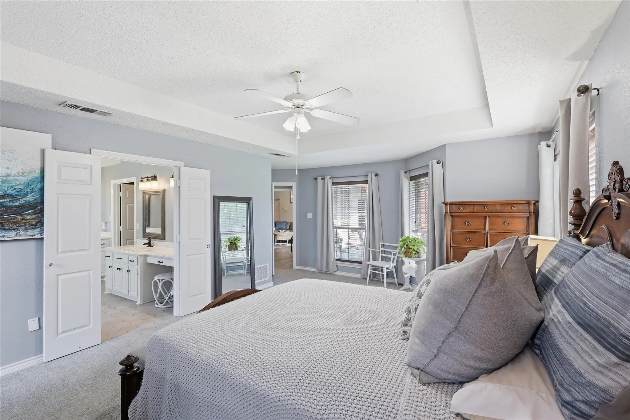 Recessed ceiling with ceiling fan, tray ceiling, and bay window featuring horizontal blinds and curtains