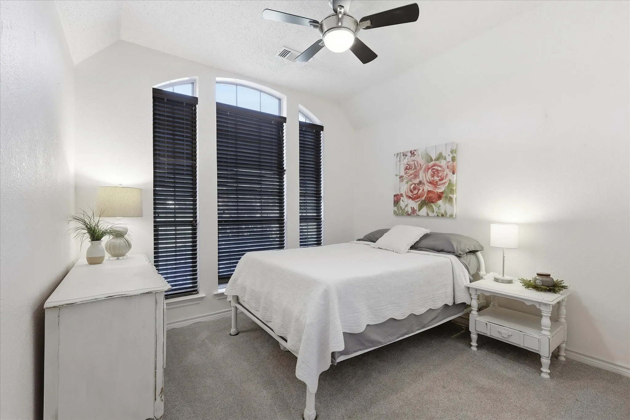 Room featuring vaulted ceiling, arched windows with dark horizontal blinds, and neutral carpet