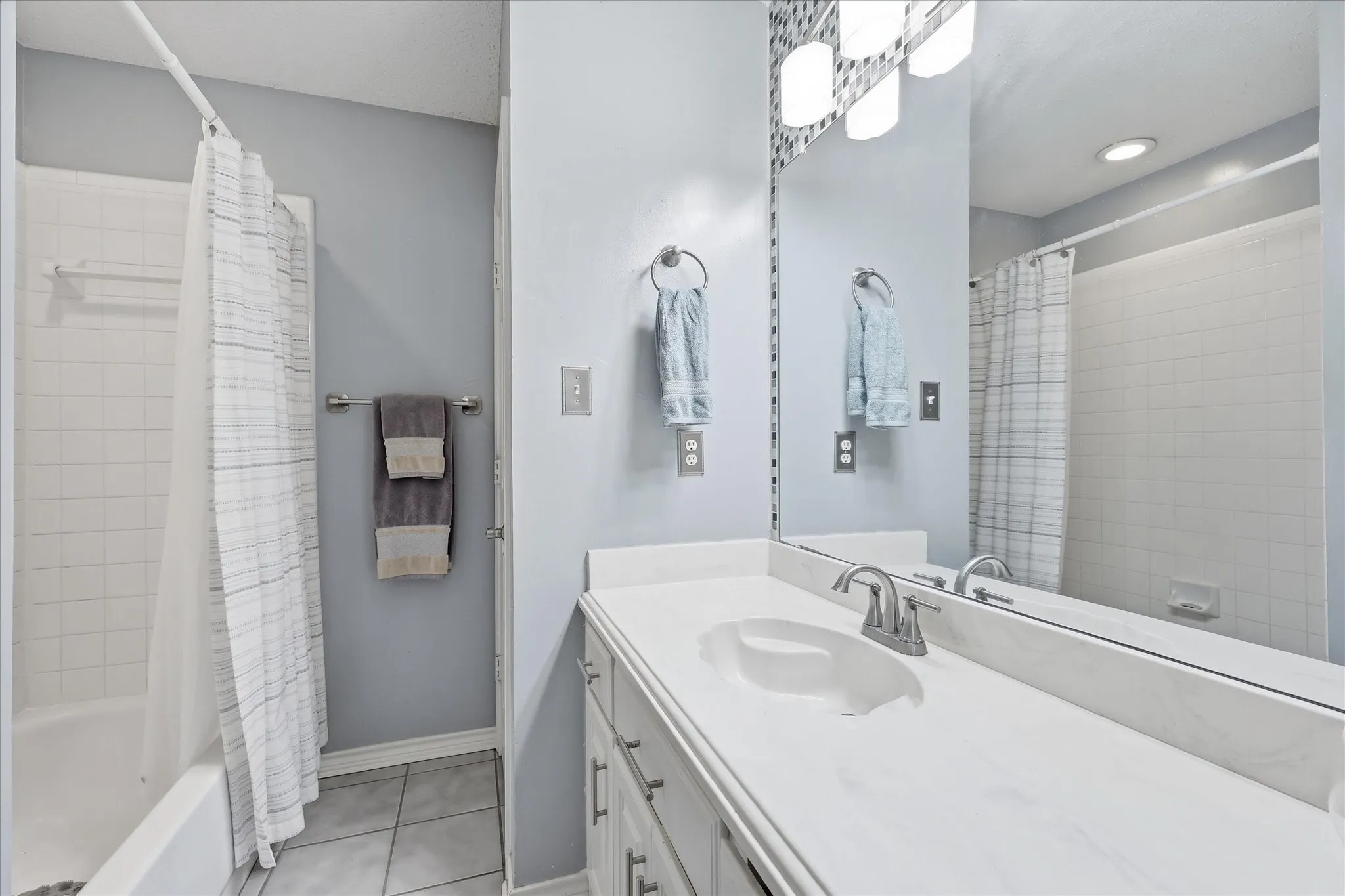 Bathroom vanity featuring a white countertop with an integrated sink, brushed nickel faucet, and a large mirror with overhead lighting