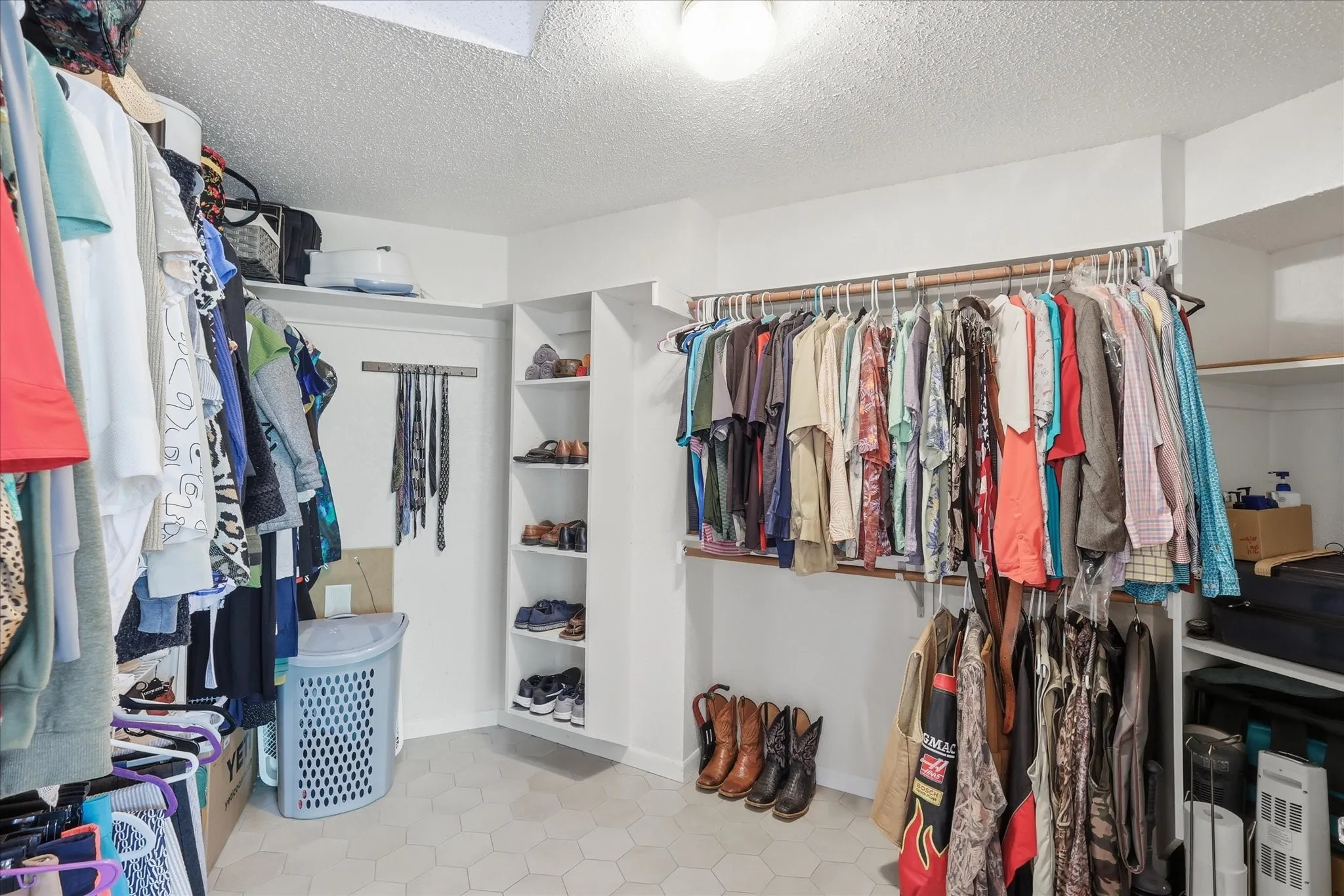 Expansive walk-in closet featuring white walls, overhead lighting, and hexagonal tile flooring