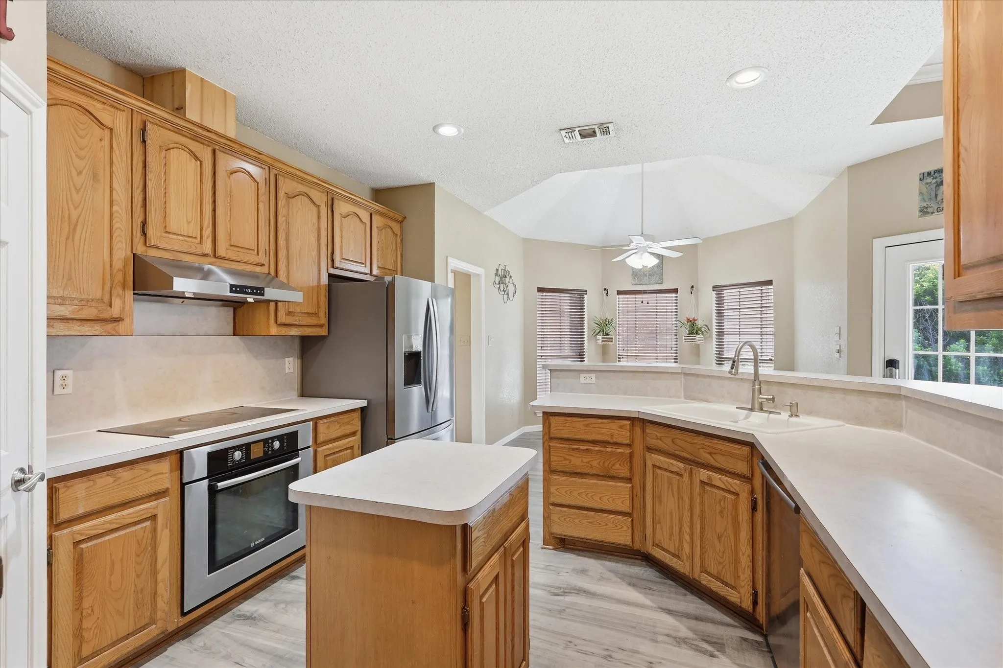 Well-appointed kitchen featuring light wood cabinetry, stainless steel appliances, a center island, light countertops, and wood-finish flooring
