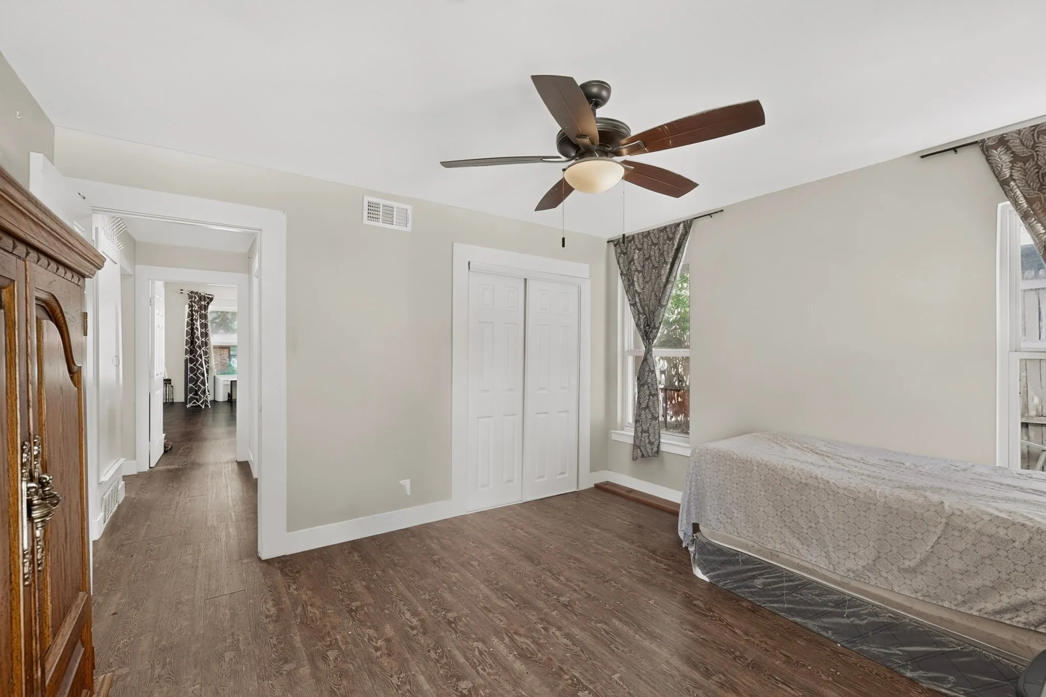 Room featuring wood-finish flooring, a ceiling fan with light fixture, and white bi-fold closet doors