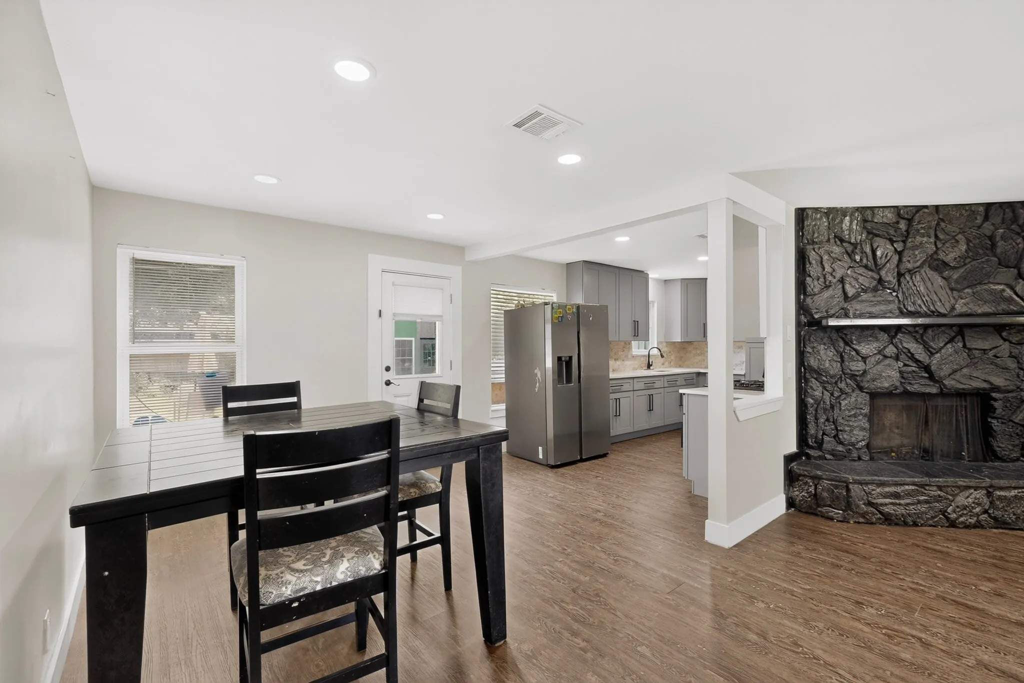 Living area featuring a stone fireplace with a raised hearth, wood-finish flooring, and recessed lighting