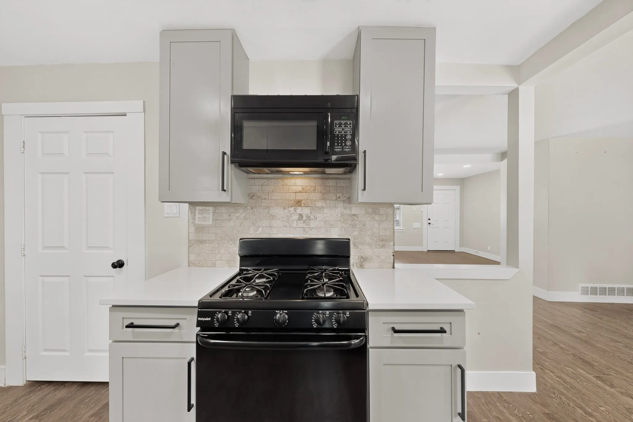 Kitchen featuring light grey cabinetry, white countertops, black oven with gas cooktop, black built-in microwave, and light-toned tile backsplash