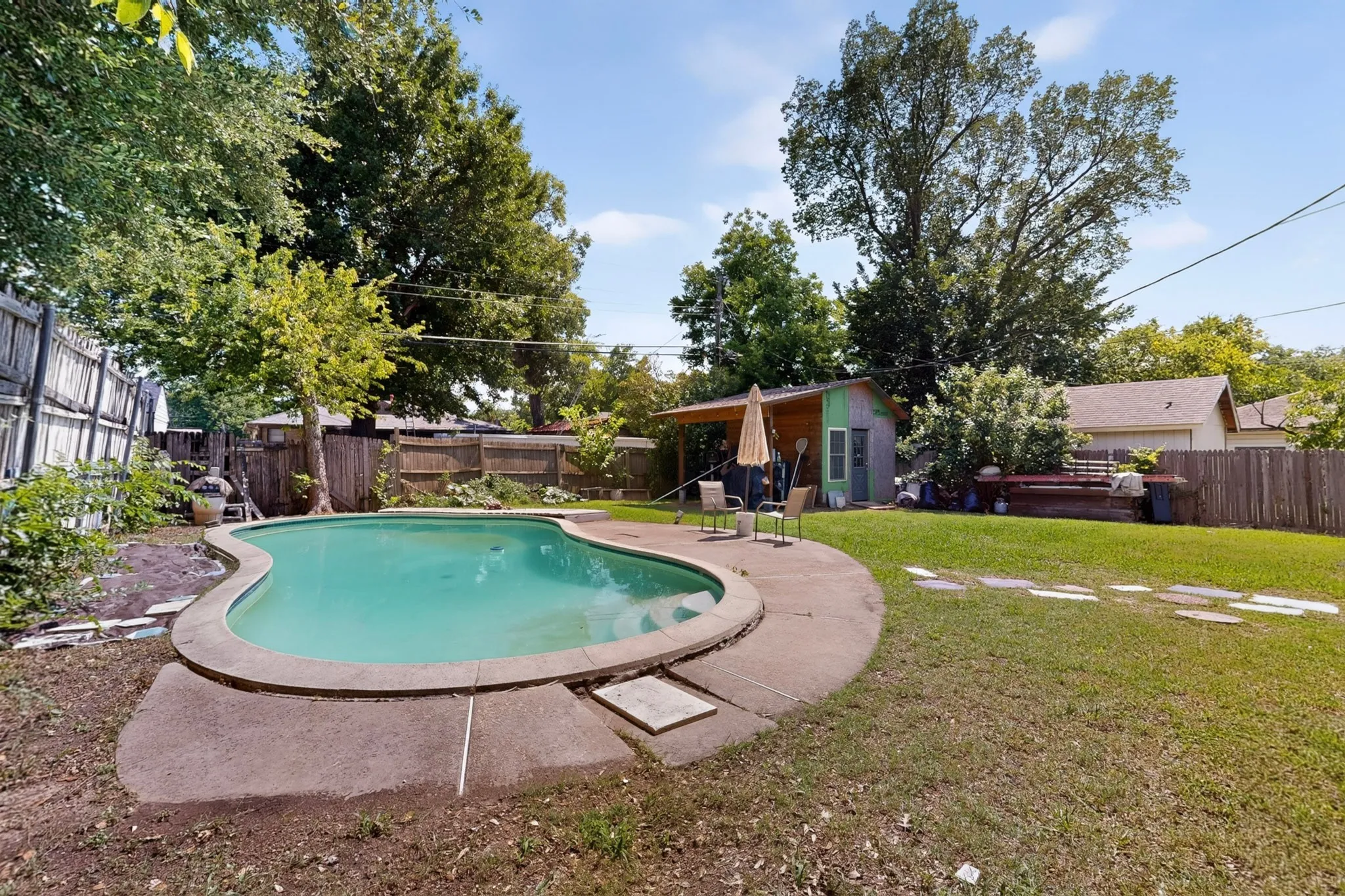 Backyard featuring a free-form swimming pool with concrete coping, a covered patio area, and a utility shed
