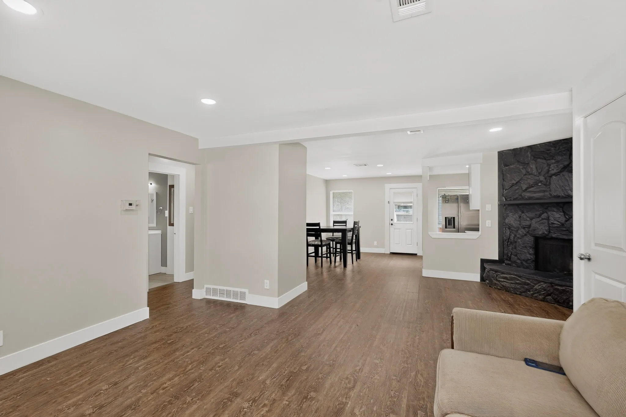 Open-concept living area featuring wood-finish flooring, recessed lighting, and a textured black stone fireplace