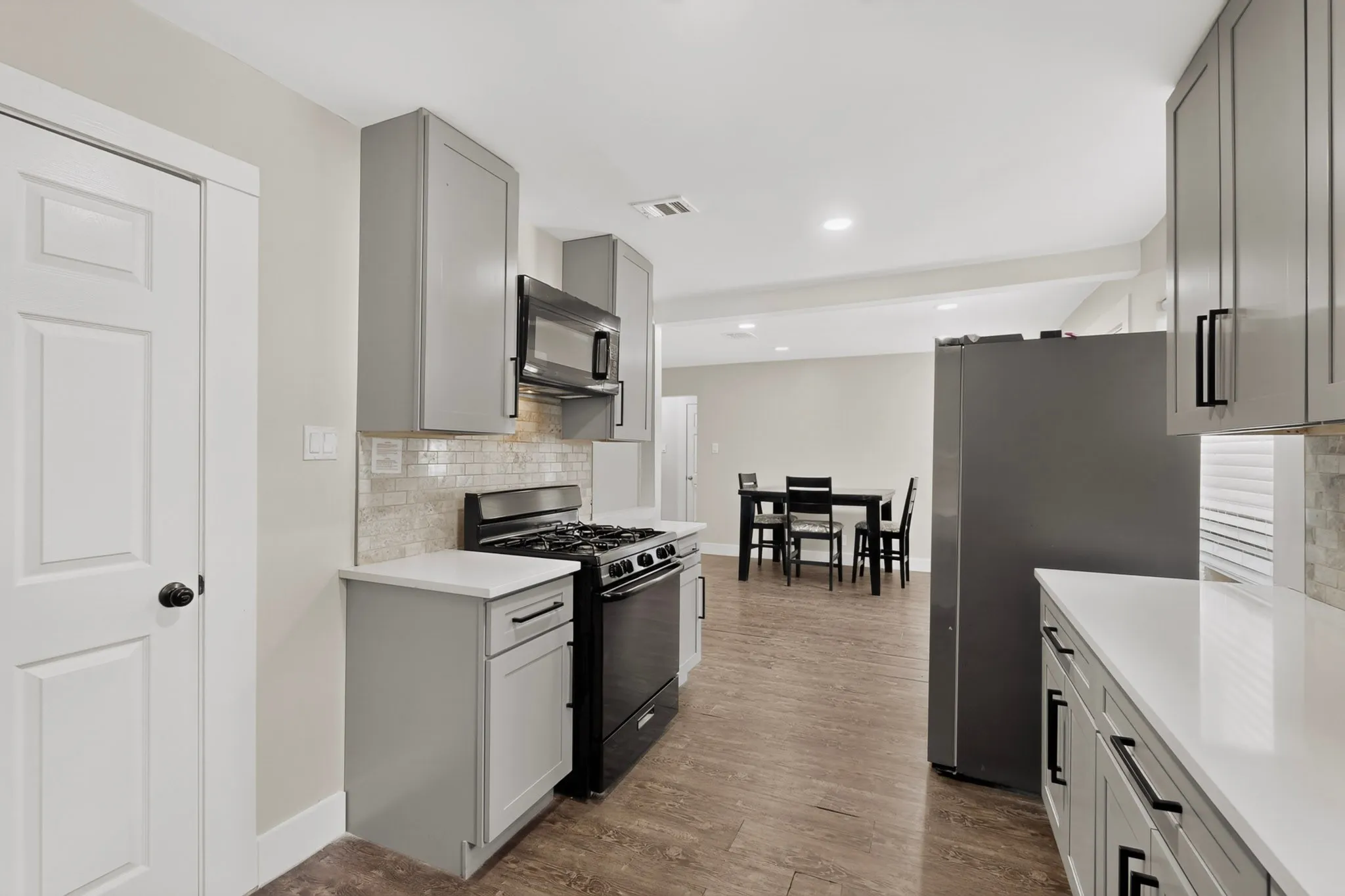 Modern kitchen featuring grey shaker-style cabinetry with matte black hardware, white countertops, and a subway tile backsplash