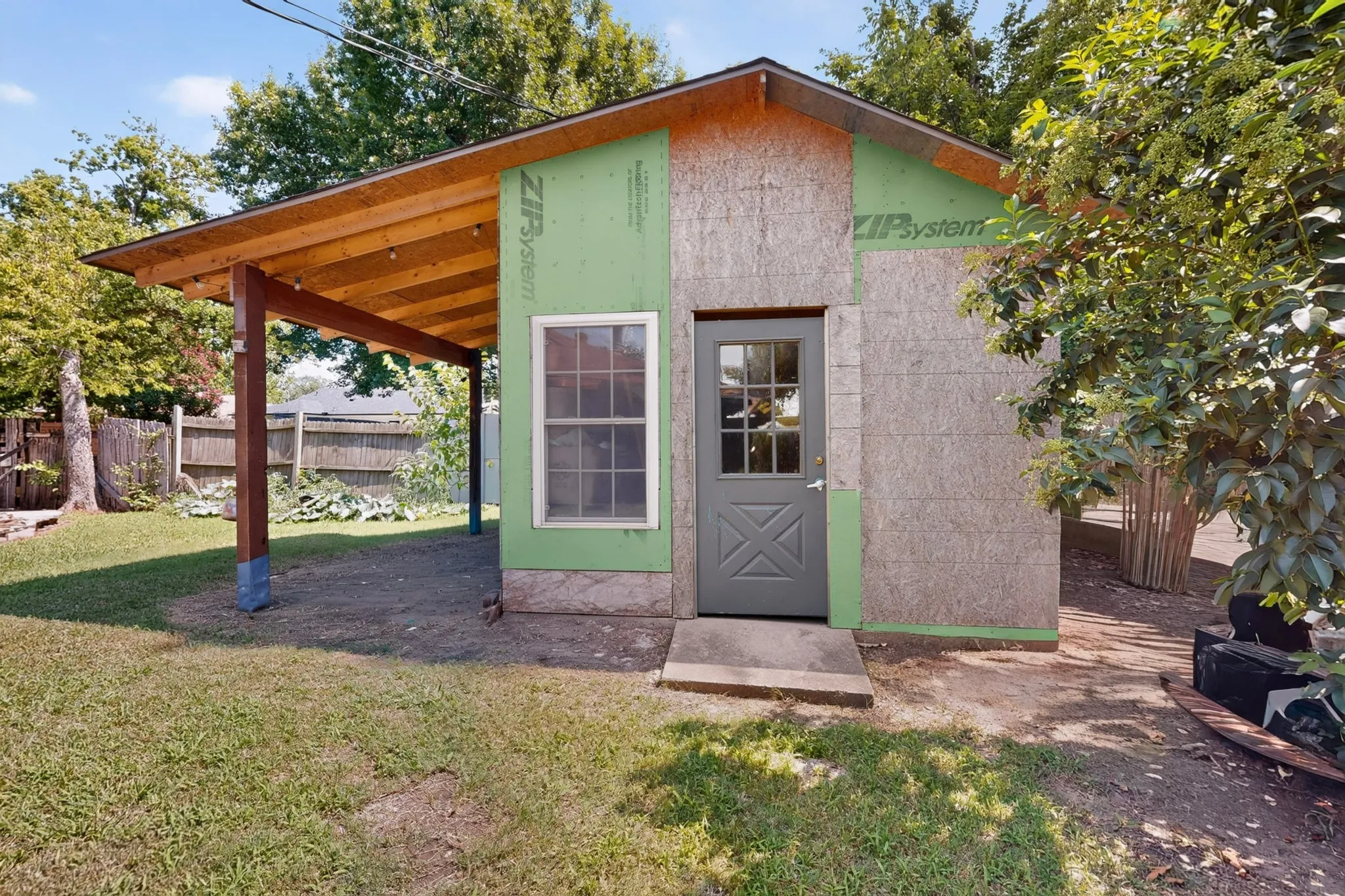 Exterior structure featuring an unfinished facade, a covered patio area with exposed rafters, and a gray paneled door with window lites