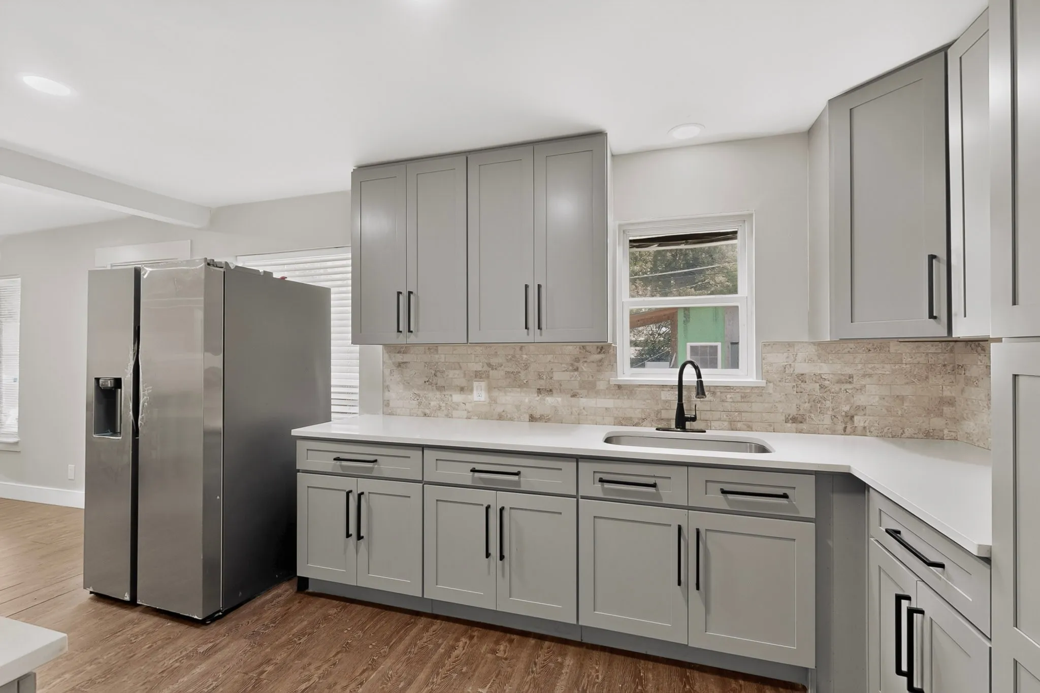 Modern kitchen featuring light gray shaker cabinetry with matte black hardware, white countertops, and a stone-look backsplash