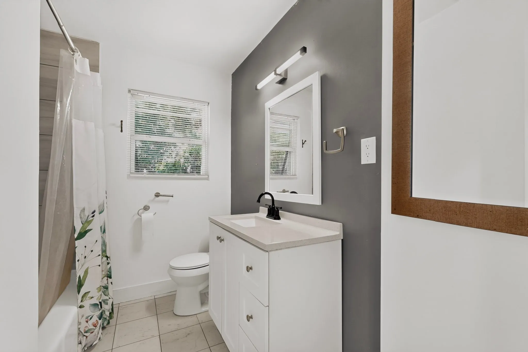 White vanity with a light countertop, black faucet, and white framed mirror