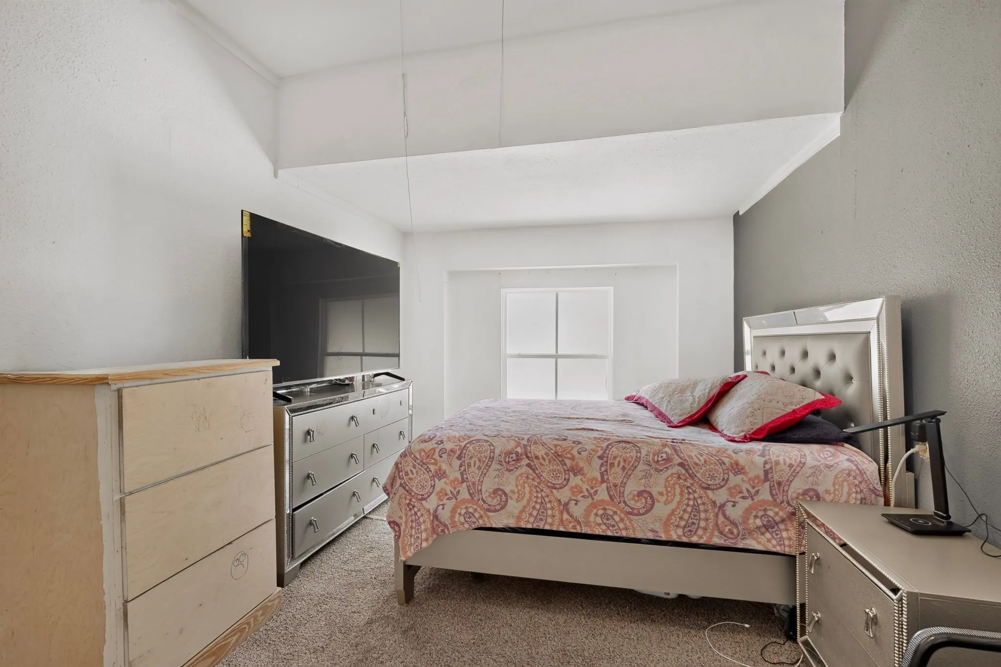 Bedroom featuring textured gray accent wall and light-colored carpeting