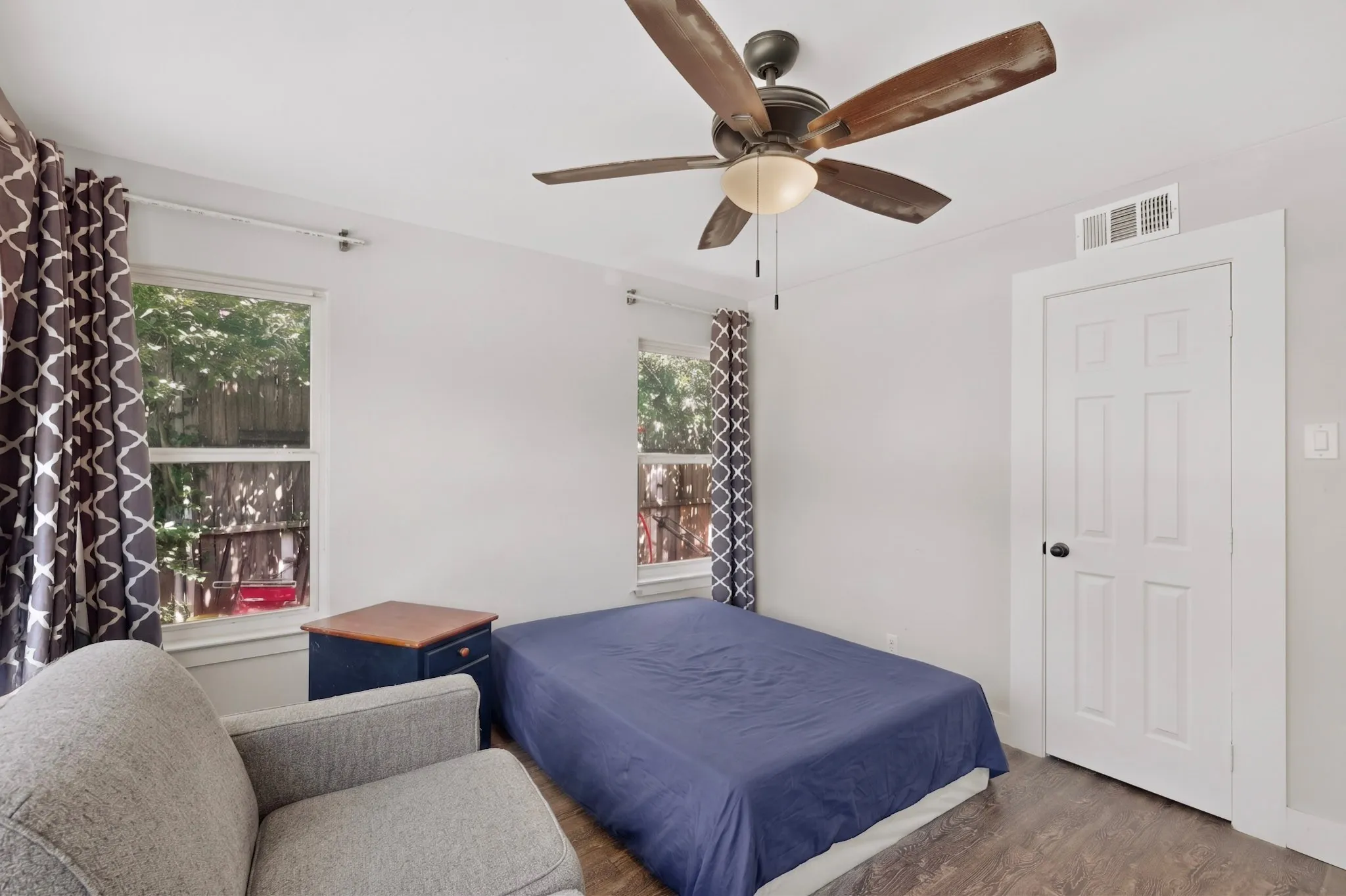 Room featuring wood-finish flooring, two large windows, a ceiling fan with light fixture, and a white paneled door with dark hardware