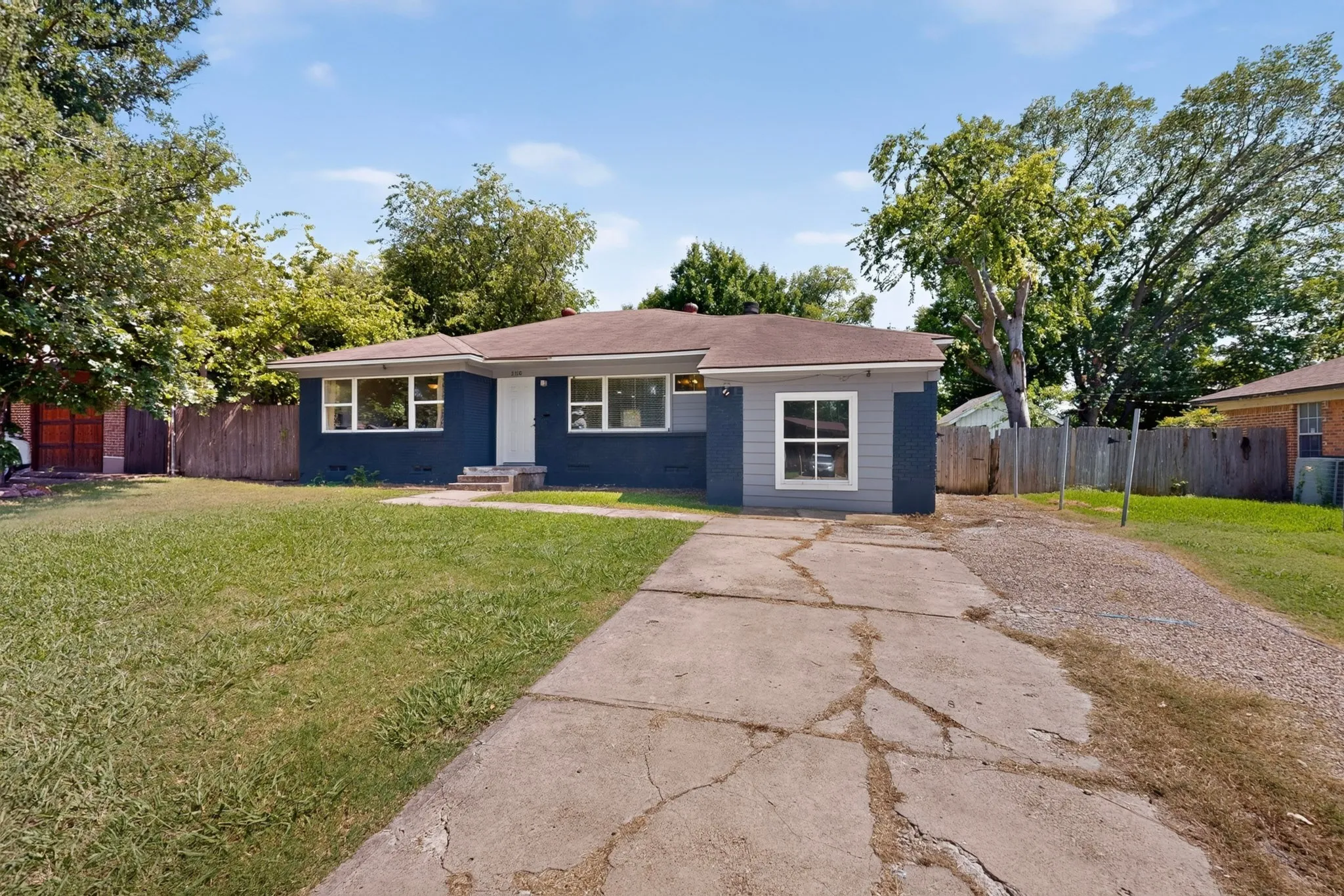 Single-story residence featuring a dark blue facade with light gray accents, white-trimmed windows, a white front entry door, and a concrete driveway