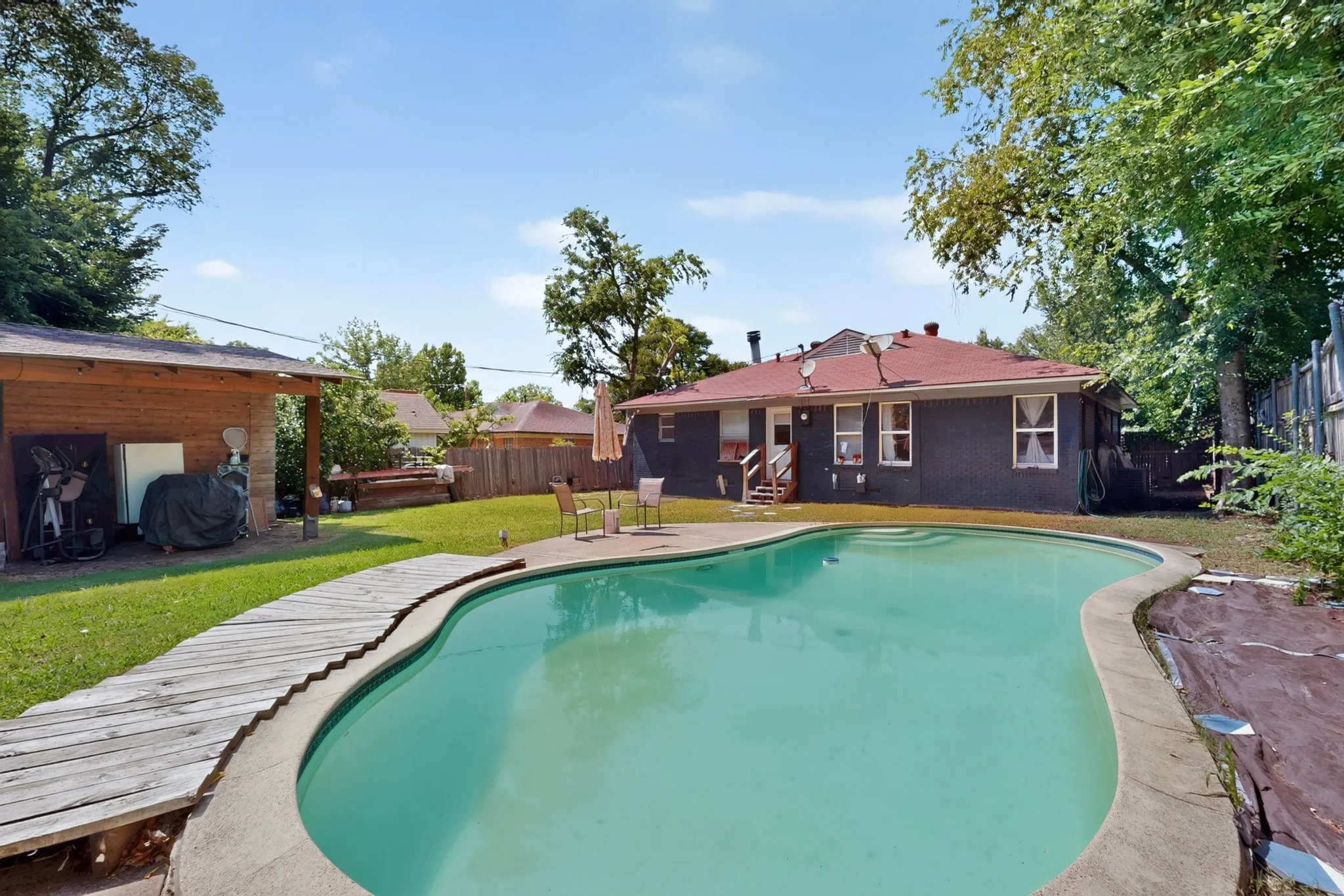 Backyard oasis featuring a curvilinear swimming pool, concrete coping, and a wooden walkway